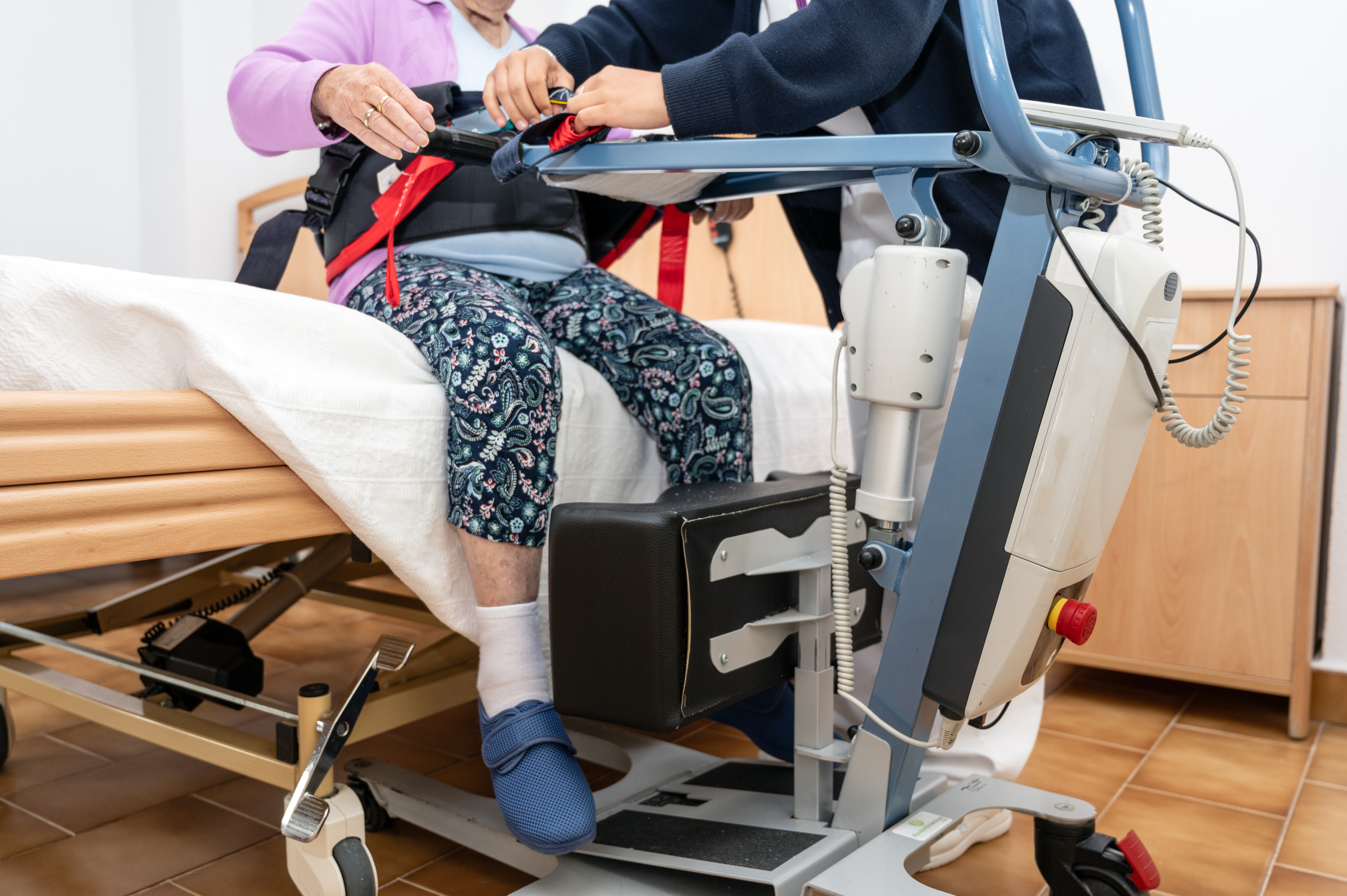 a care staff using a power assist to lifts a patie d083dfd74b878f2a09cc