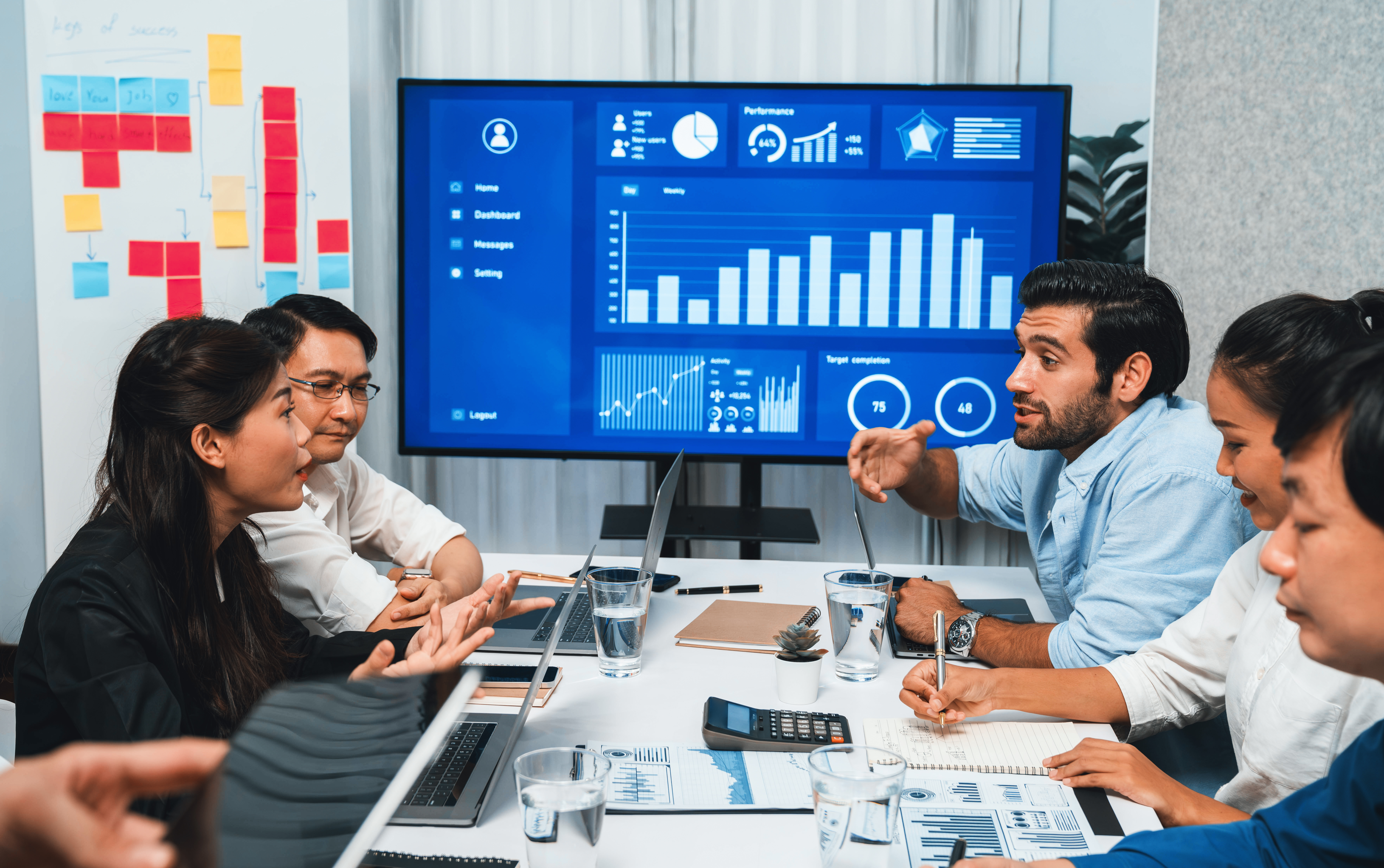 Team collaborating in a meeting, analyzing data on a screen with performance metrics, graphs, and charts, discussing digital advertising strategies for enhancing ROI in Australian businesses.