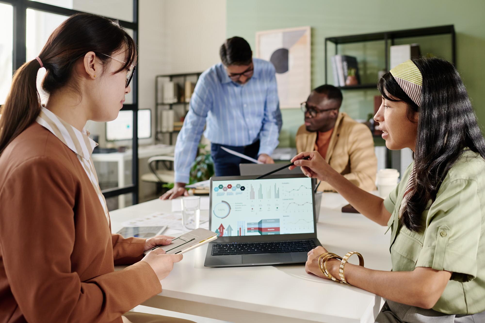 Team discussing data analytics strategies in a modern office setting, with a focus on a laptop displaying graphs and charts related to local SEO and business performance.