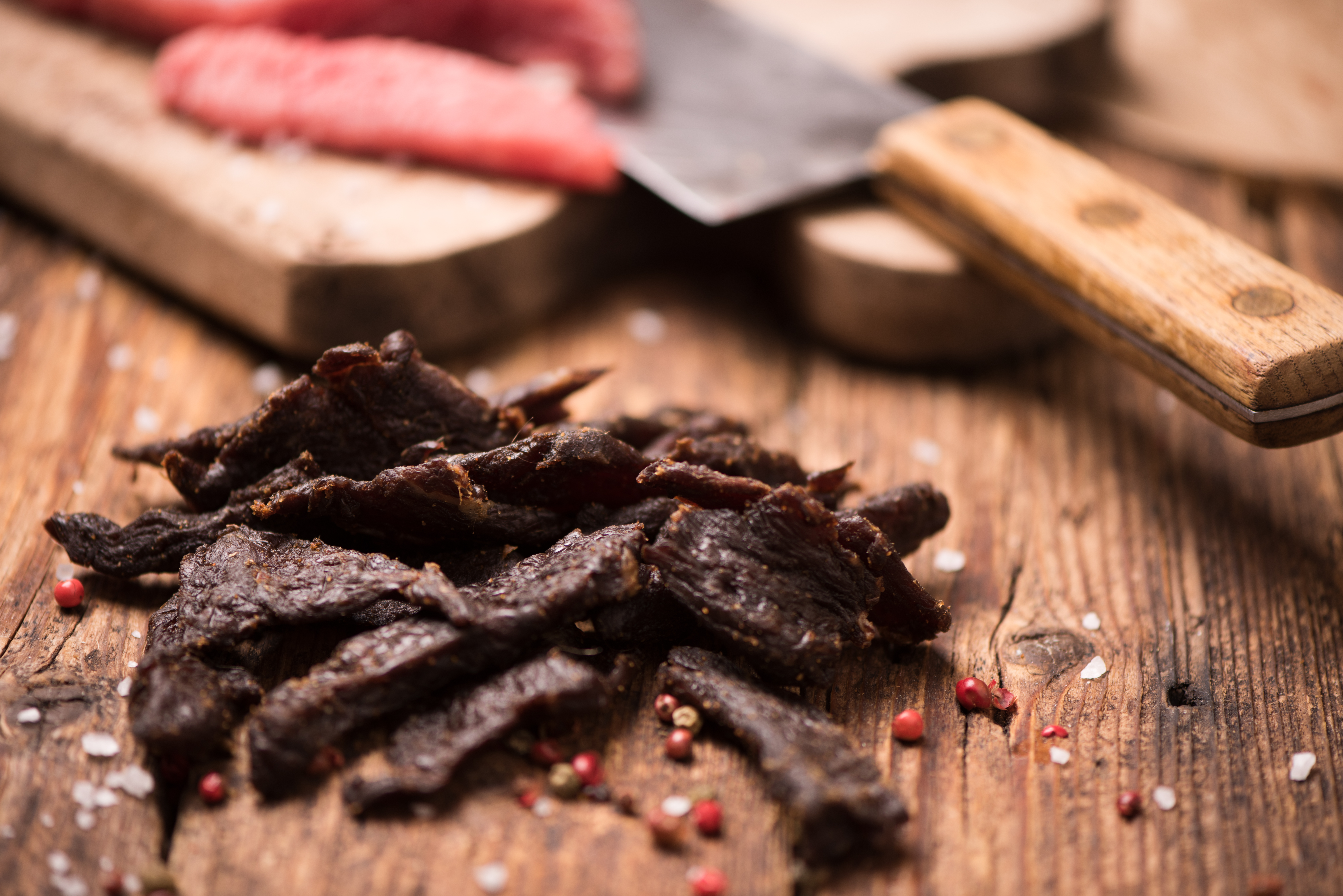 slices of beef jerky on a wooden background with a knife and spices 
