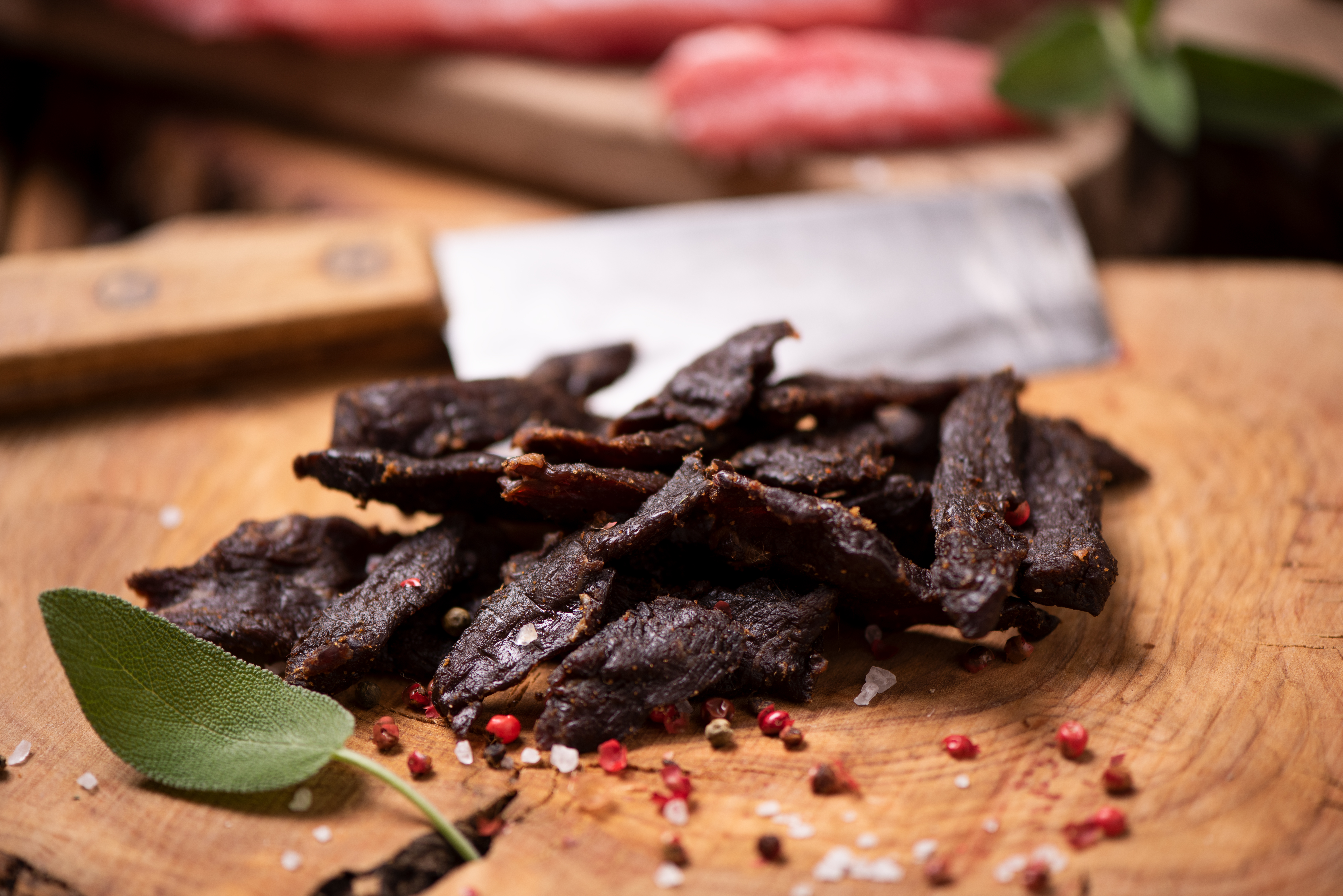 slices of beef jerky on a cutting board with spices and a cleaver