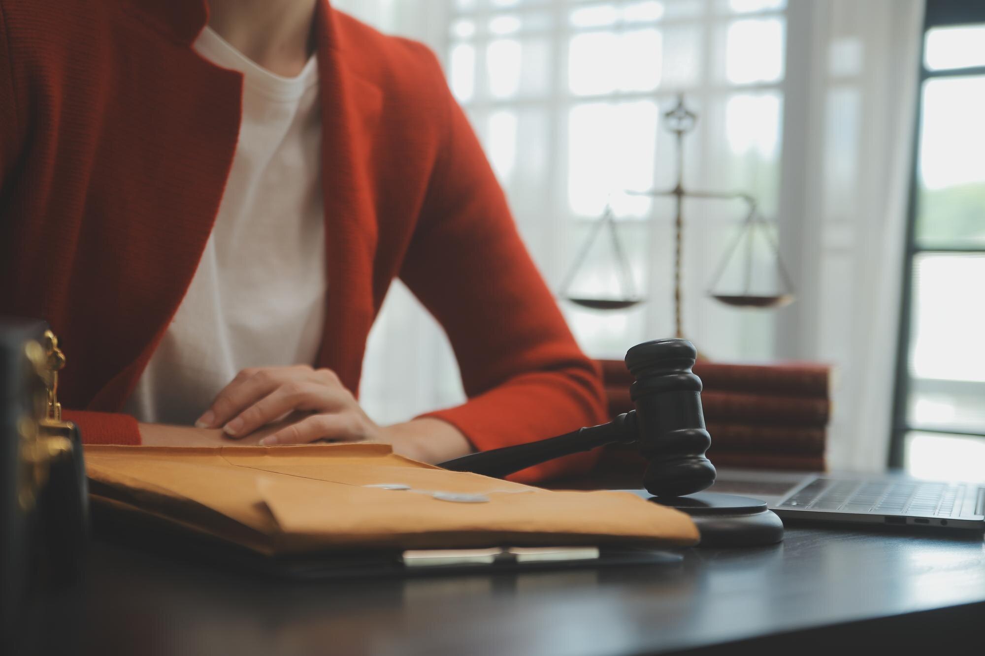 Person in Red Blazer with Legal Documents and Gavel in Office