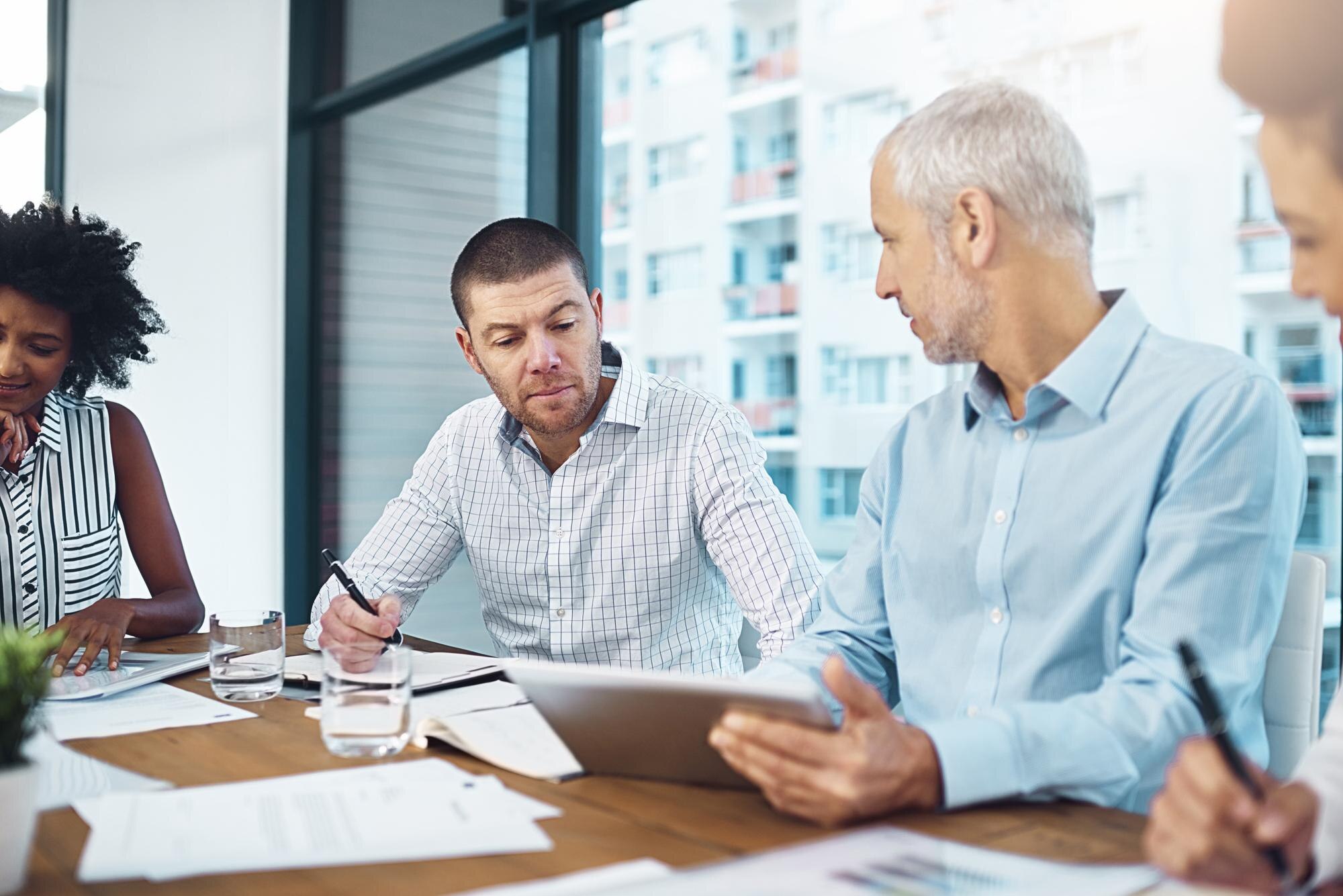 Business professionals in a boardroom reviewing commercial loan report on a tablet