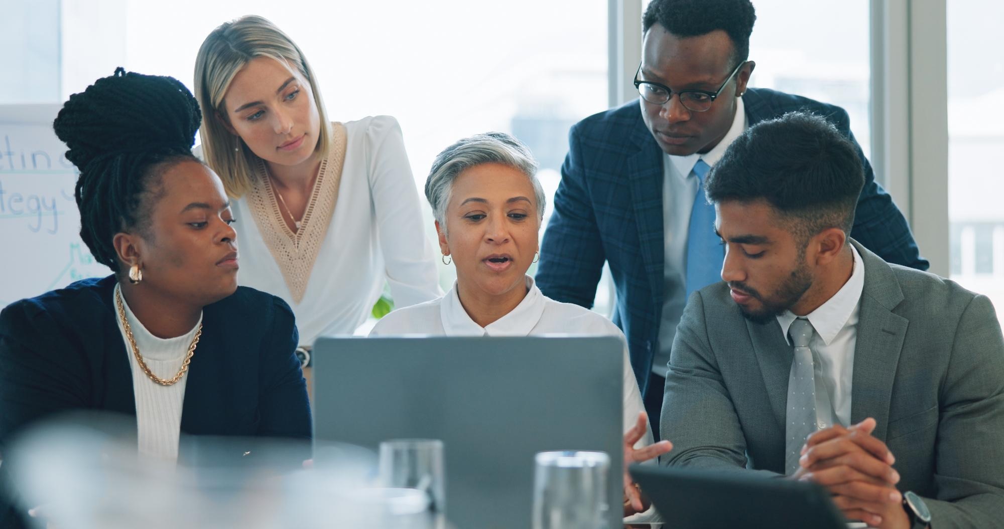 A diverse team of professionals meeting and working on a laptop.