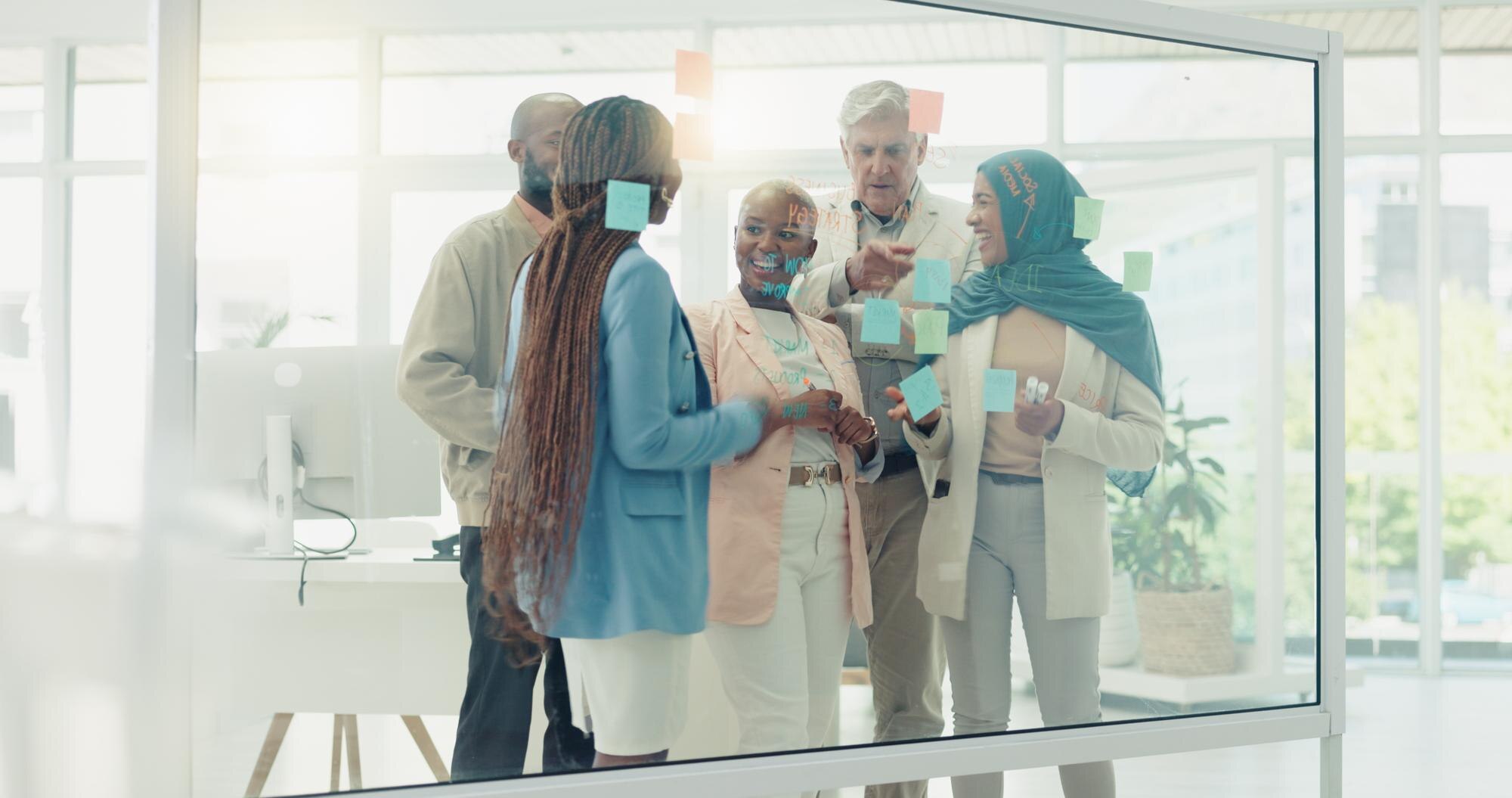 Group of diverse business professionals collaborating around a glass board with sticky notes, discussing AI strategies for optimising Google Business Profiles and enhancing local SEO.