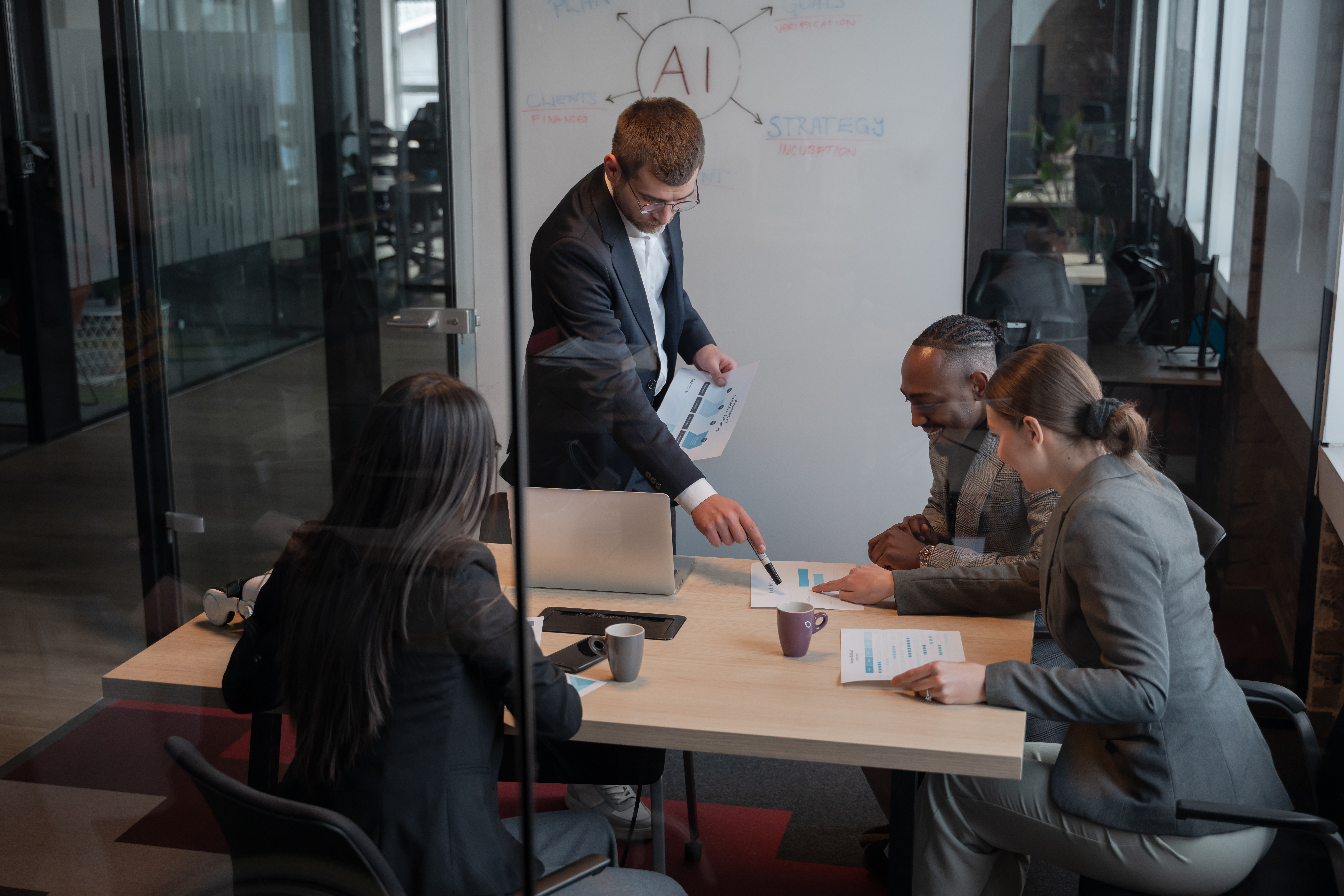 Business team in a modern office discussing AI strategies, analysing data on printed reports, and engaging in collaborative dialogue around a central table.