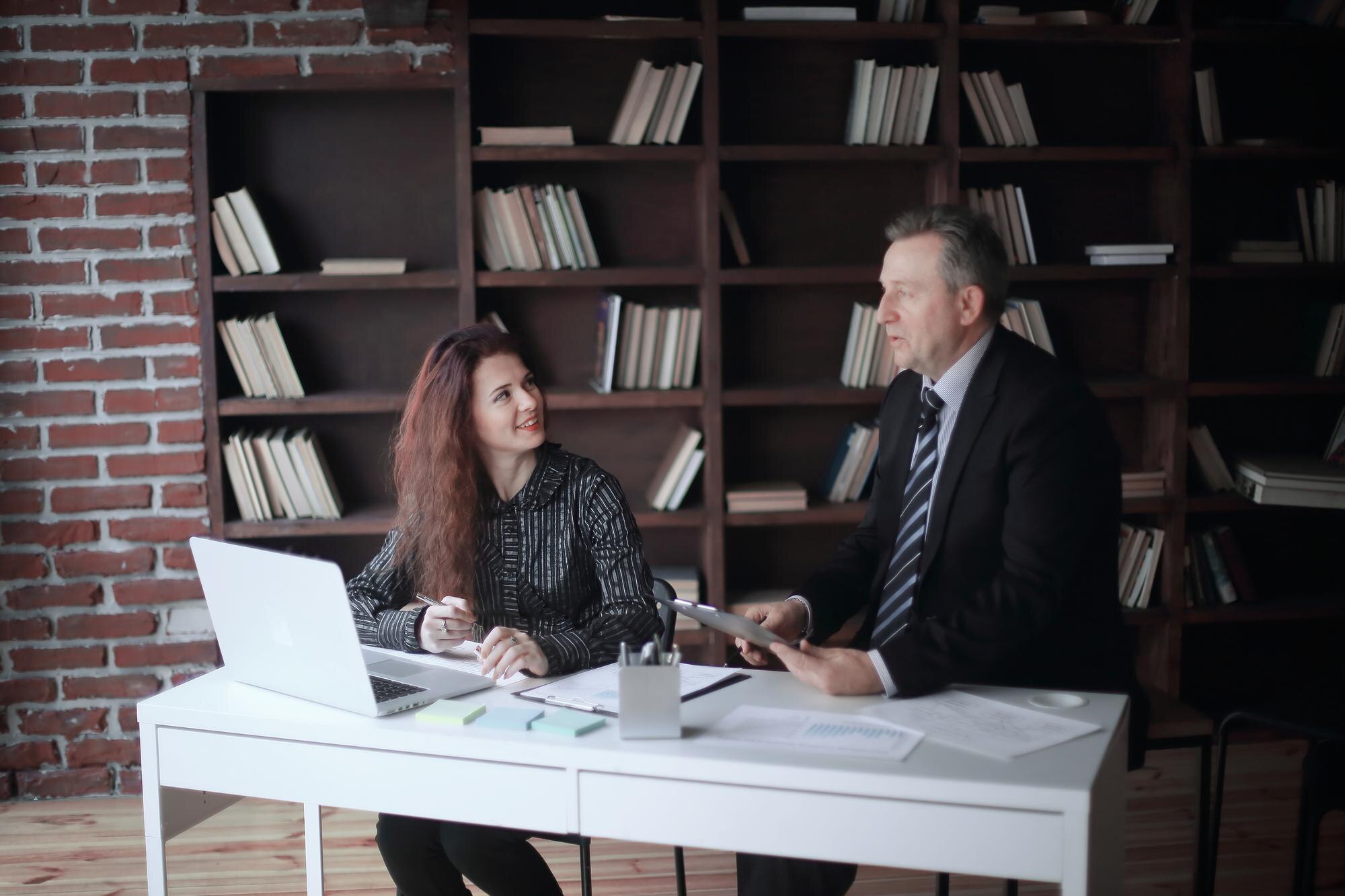 Businessman and assistant discussing legal matters in a modern office with a laptop and documents, emphasizing military divorce expertise at Coastal Virginia Law Firm.