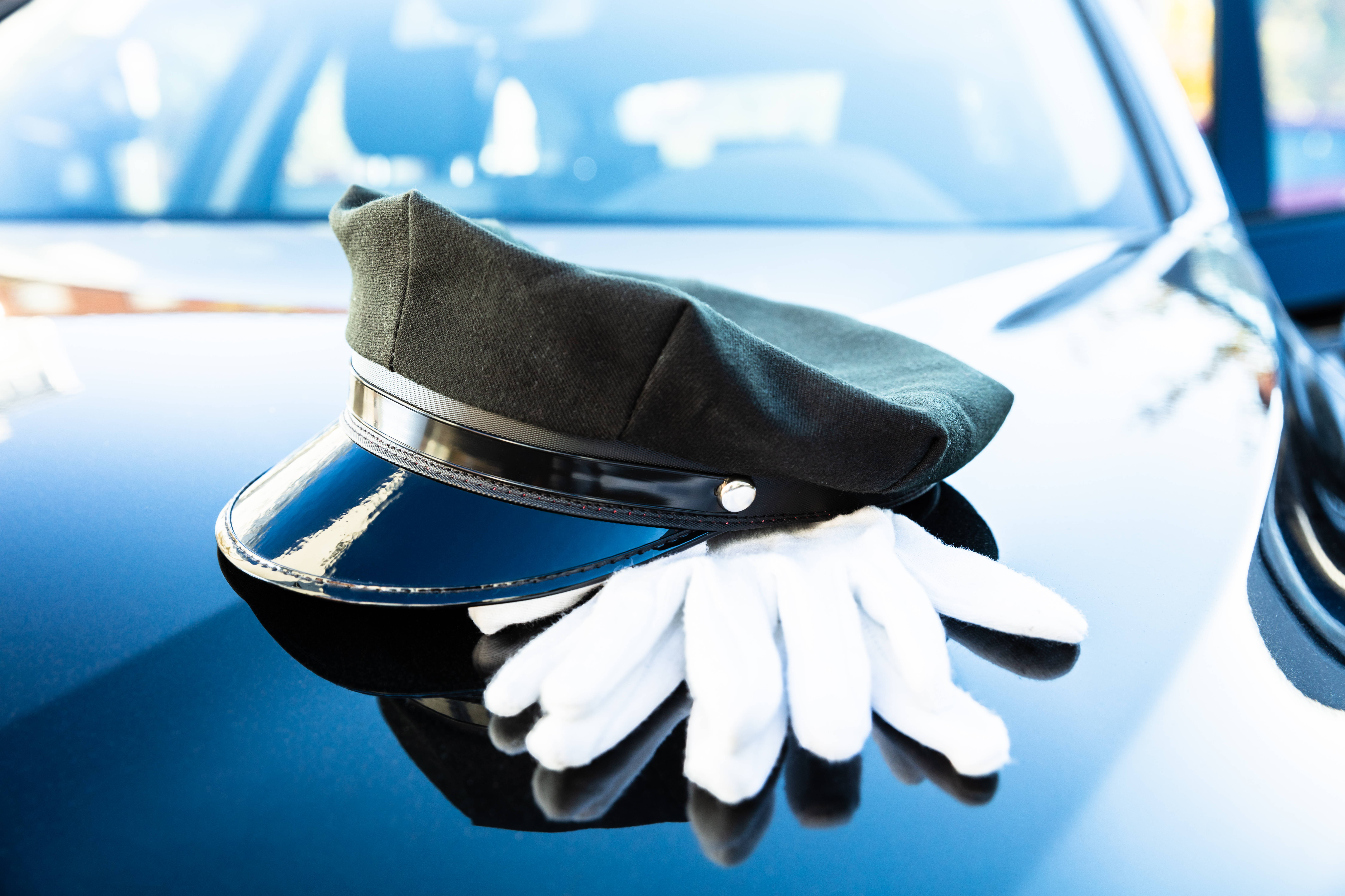 A professional black chauffeur hat and white gloves resting on a premium vehicle, representing the luxury chauffeur standards of Mak Louren.