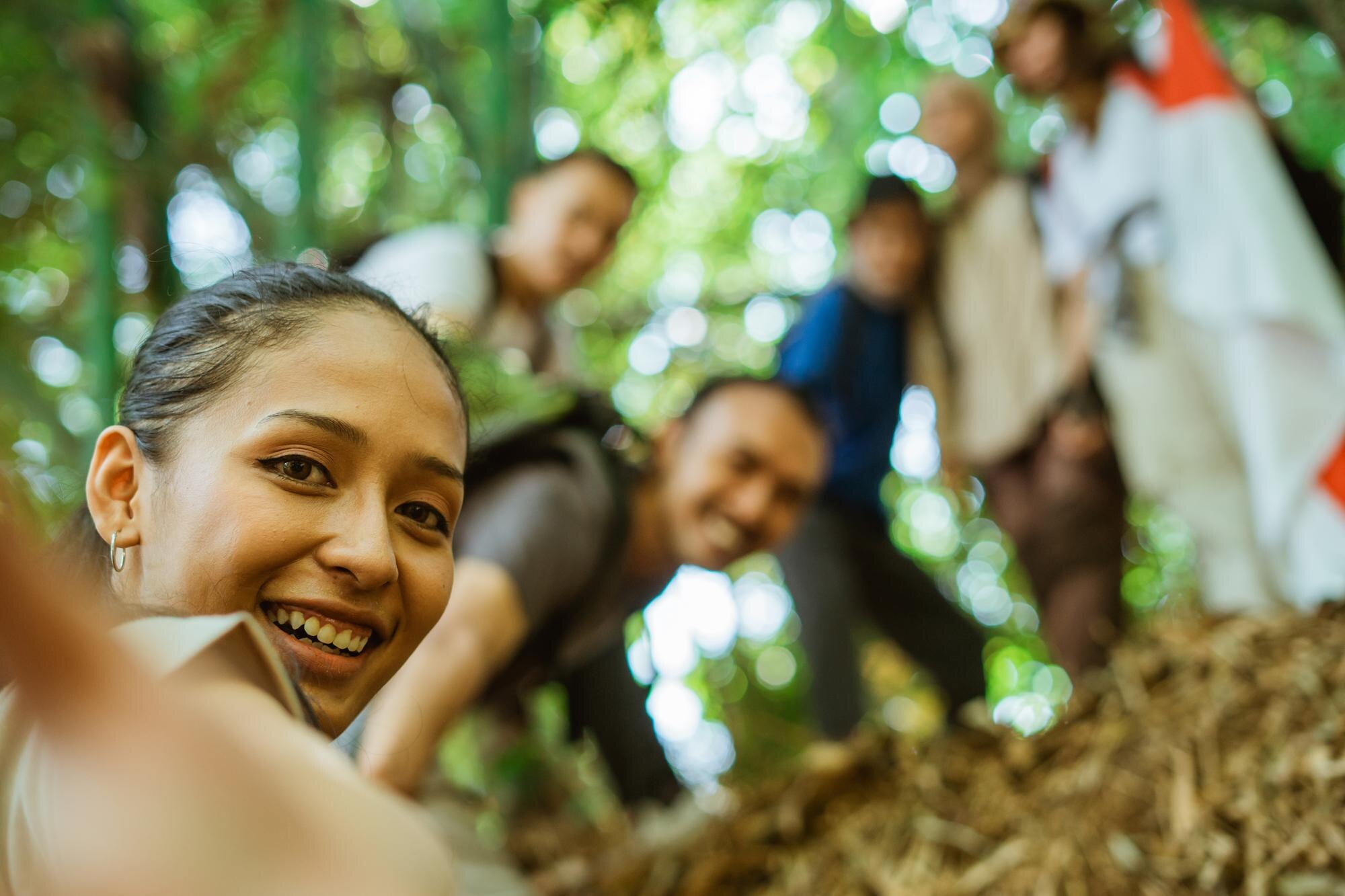 Group of friends smiling and taking a selfie while hiking together in a green forest.