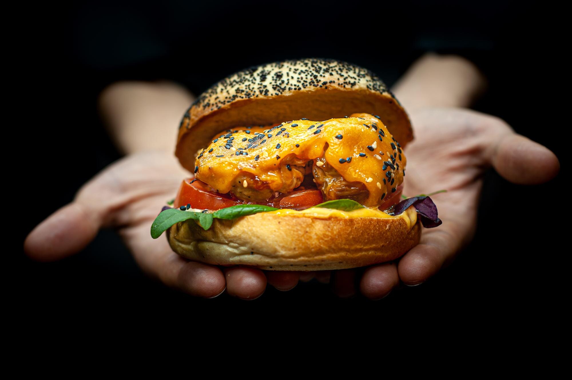 closeup of the hands holding a burger on dark back a6f9519d97ddf2ee540e