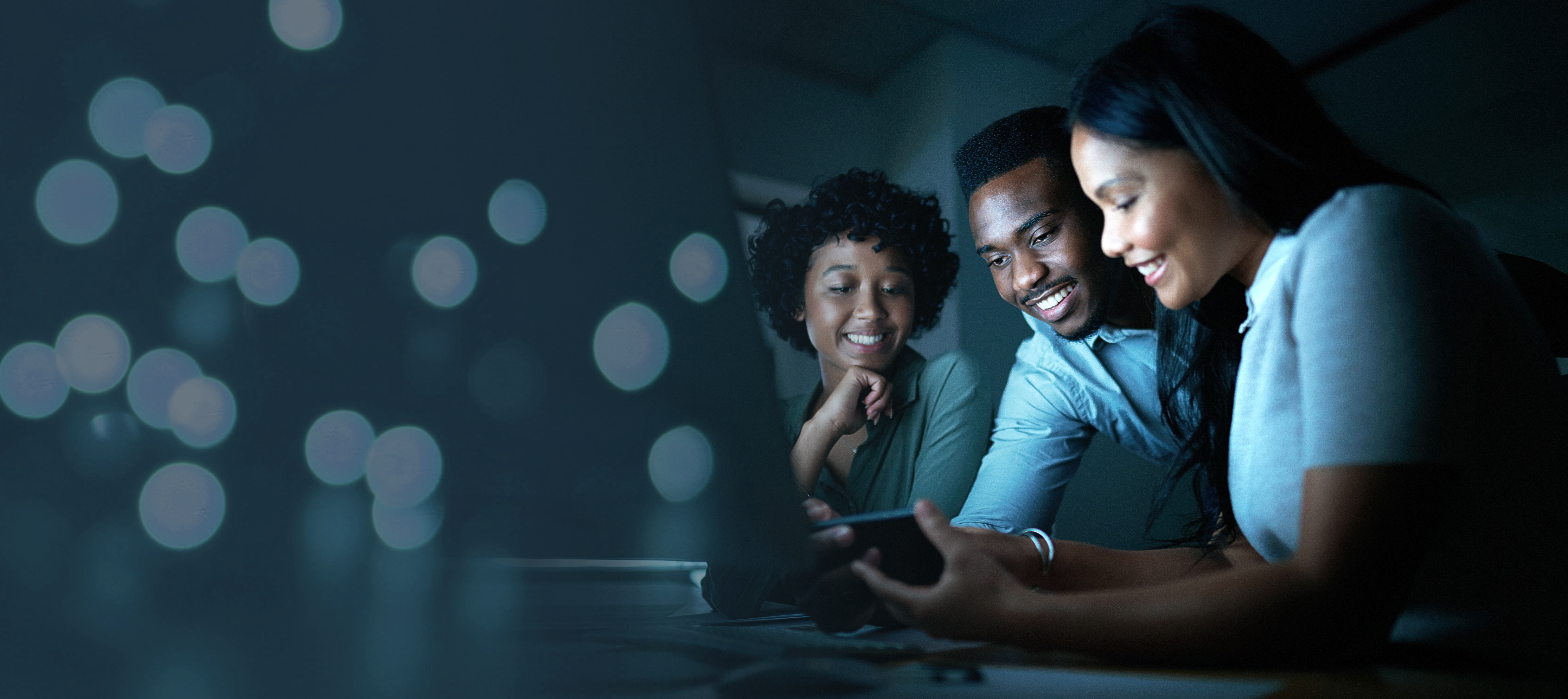 Three diverse individuals collaborating and engaging with a smartphone, illuminated by soft bokeh lights, representing teamwork and digital interaction in a business context.