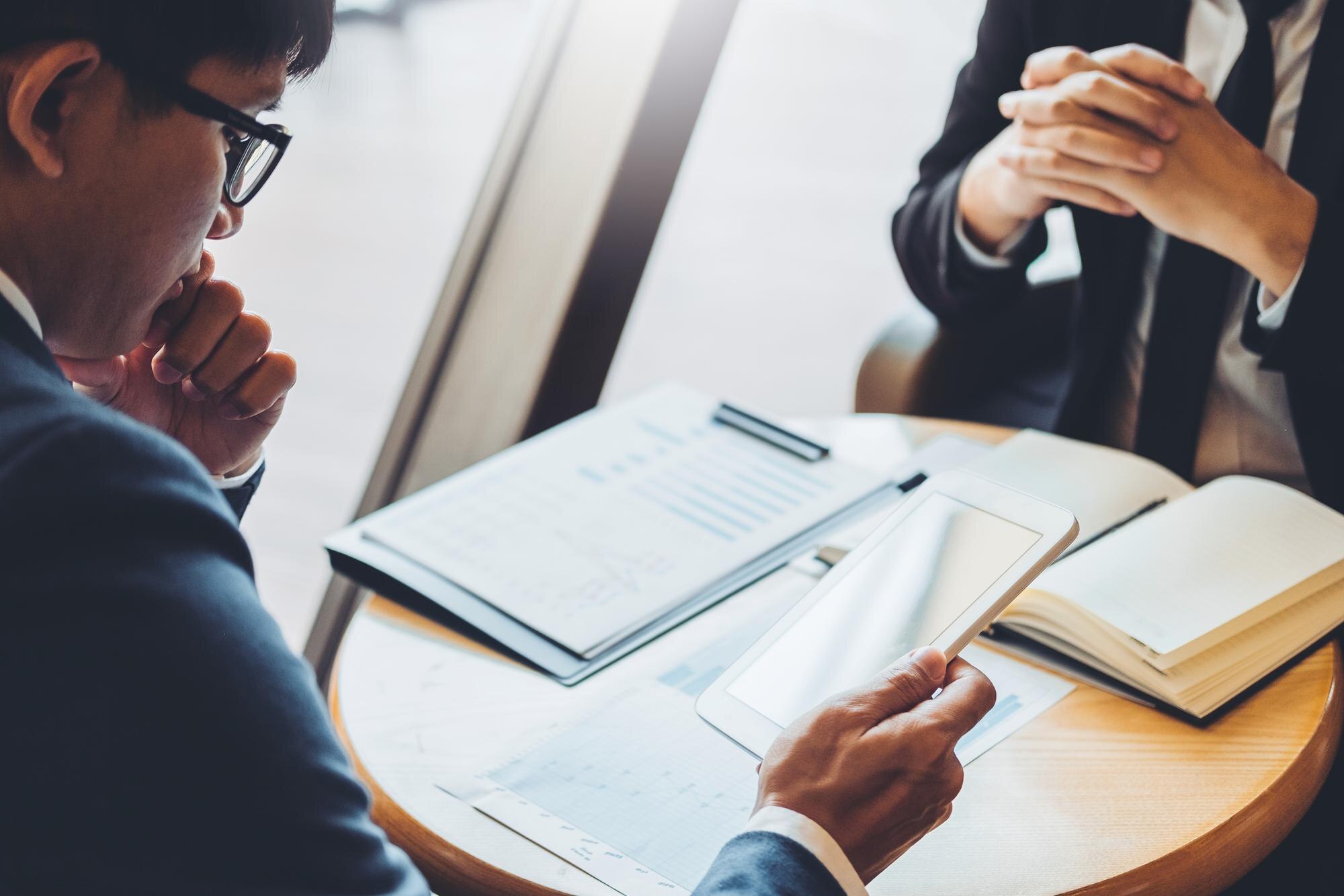 Colleagues analyzing business contracts with digital tablet and documents on a table, emphasizing the importance of clear terms and risk management.