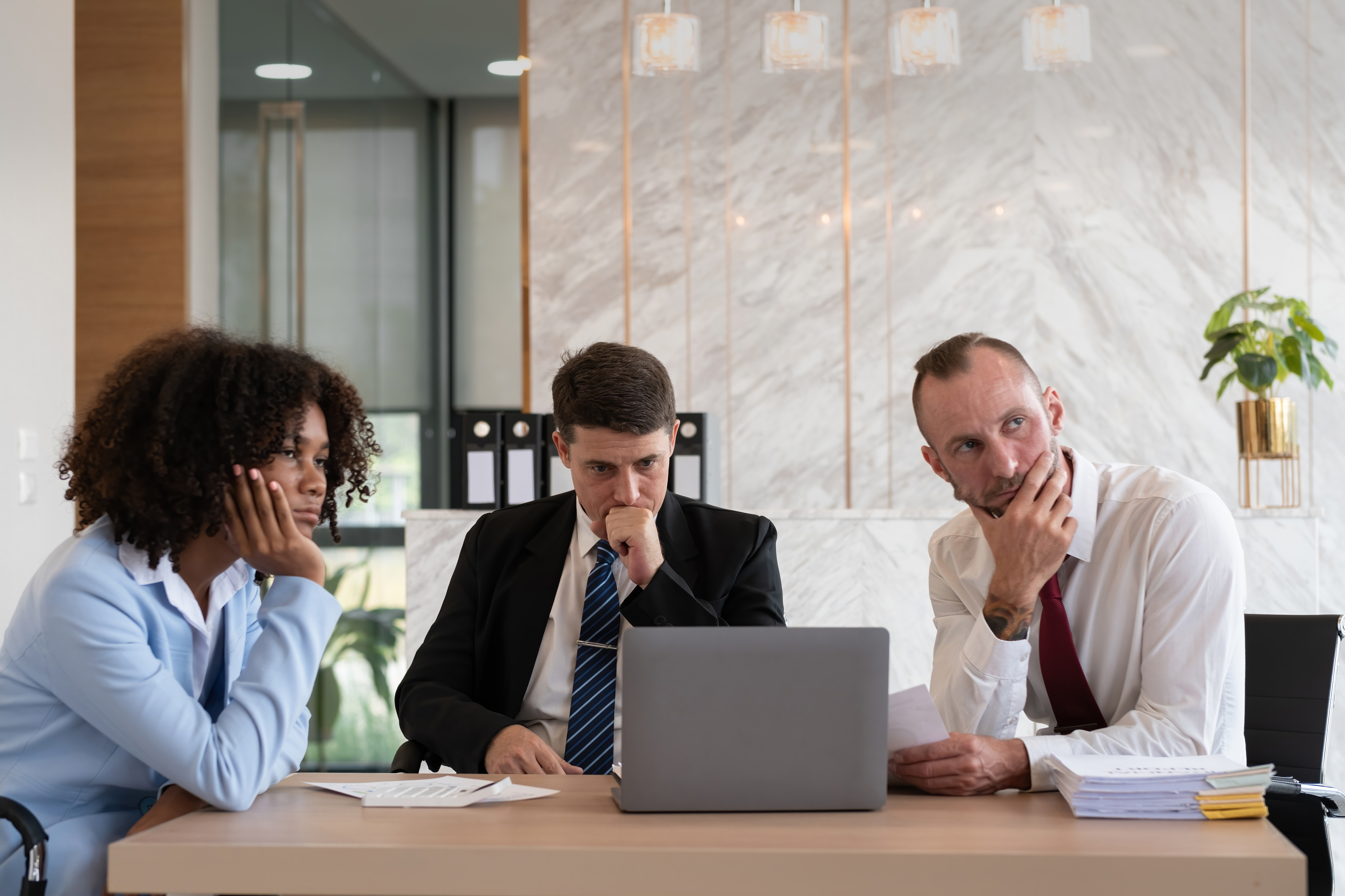 Diverse business team analysing strategies at office desk, focused on laptop and documents, reflecting on reputation management and customer engagement.