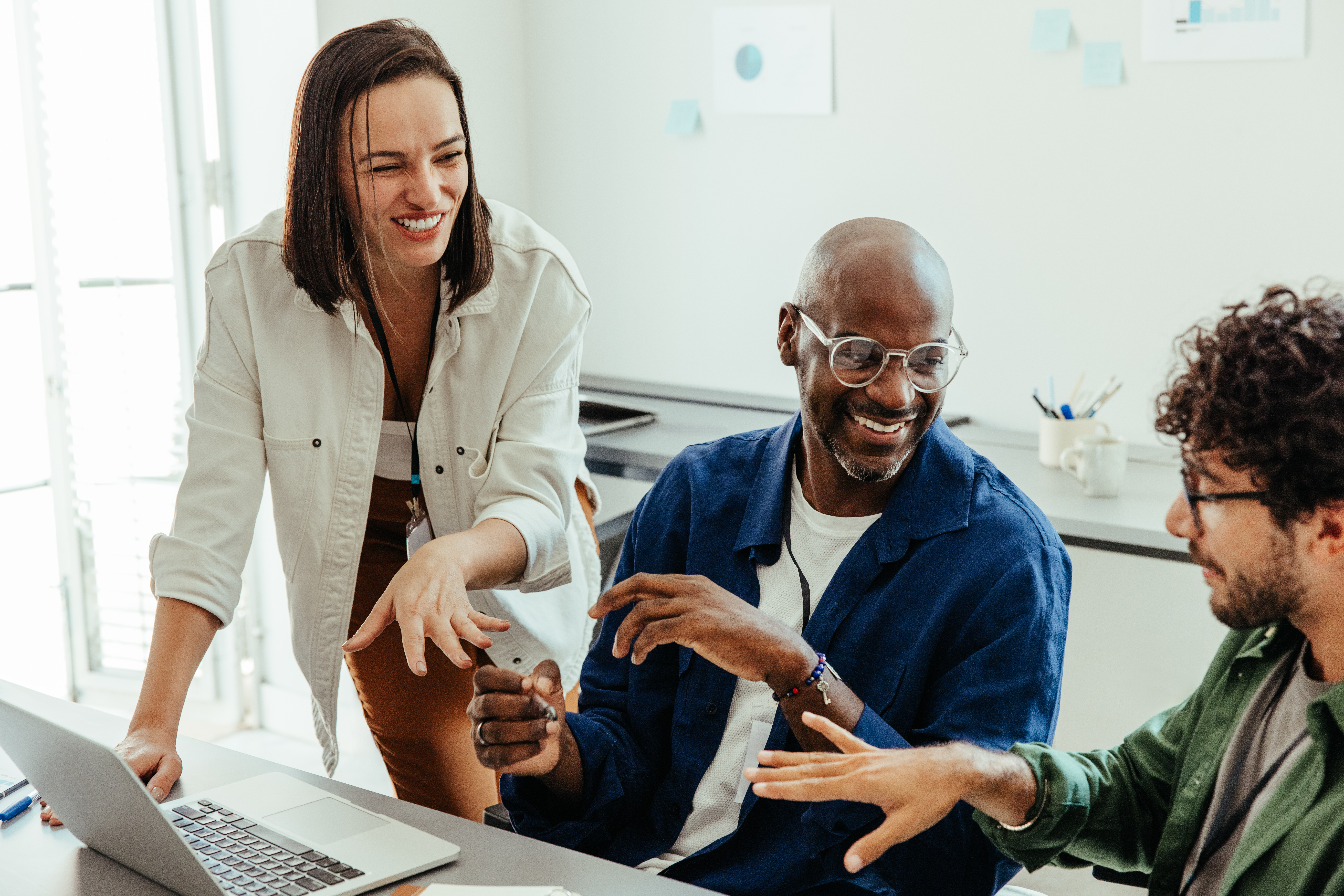 Diverse co-workers engaged in a collaborative discussion around a laptop, highlighting teamwork and communication in a professional setting.