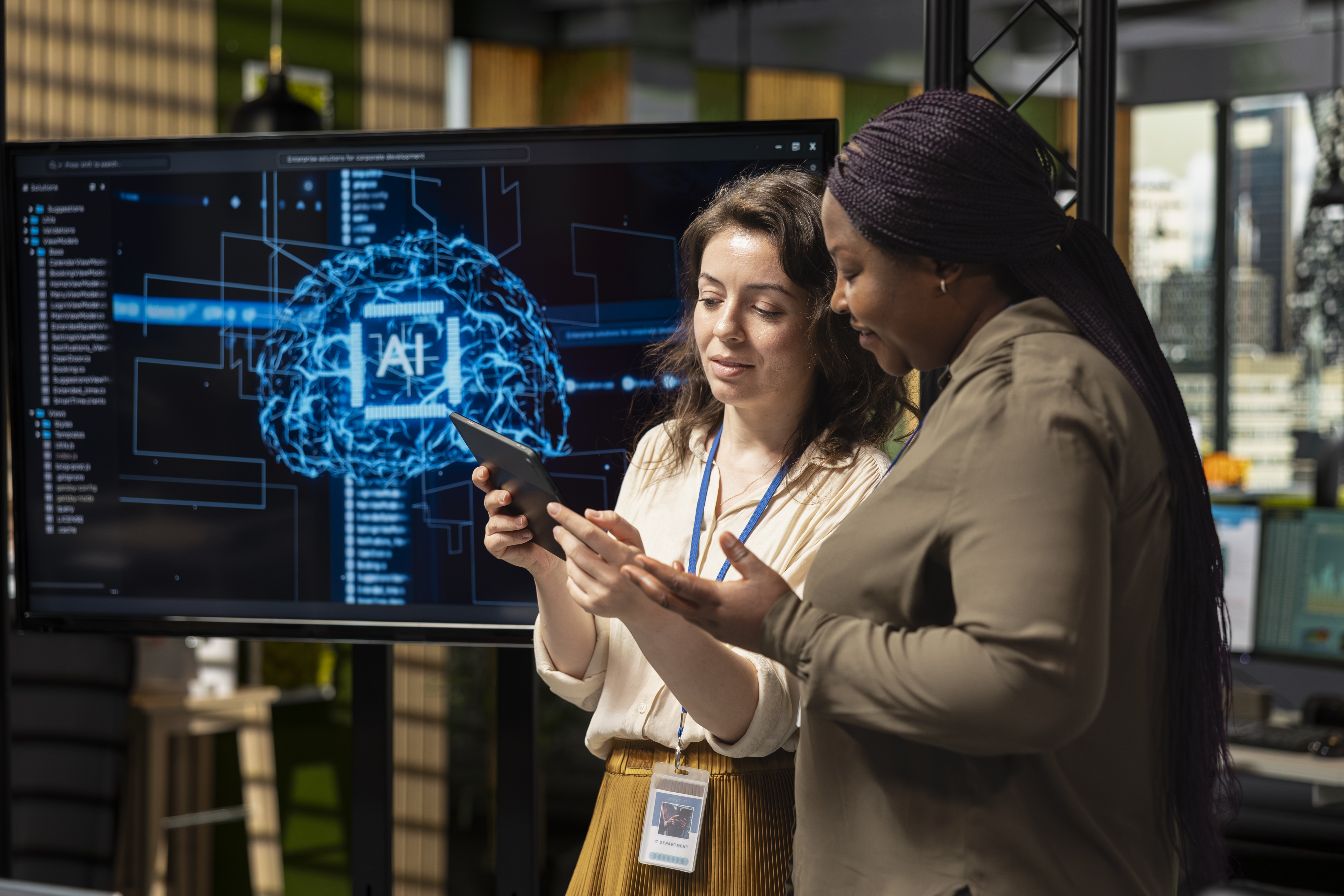 Two diverse women discussing AI-driven tools, with a digital display of an AI brain concept in the background, highlighting technology's role in enhancing business profile management.