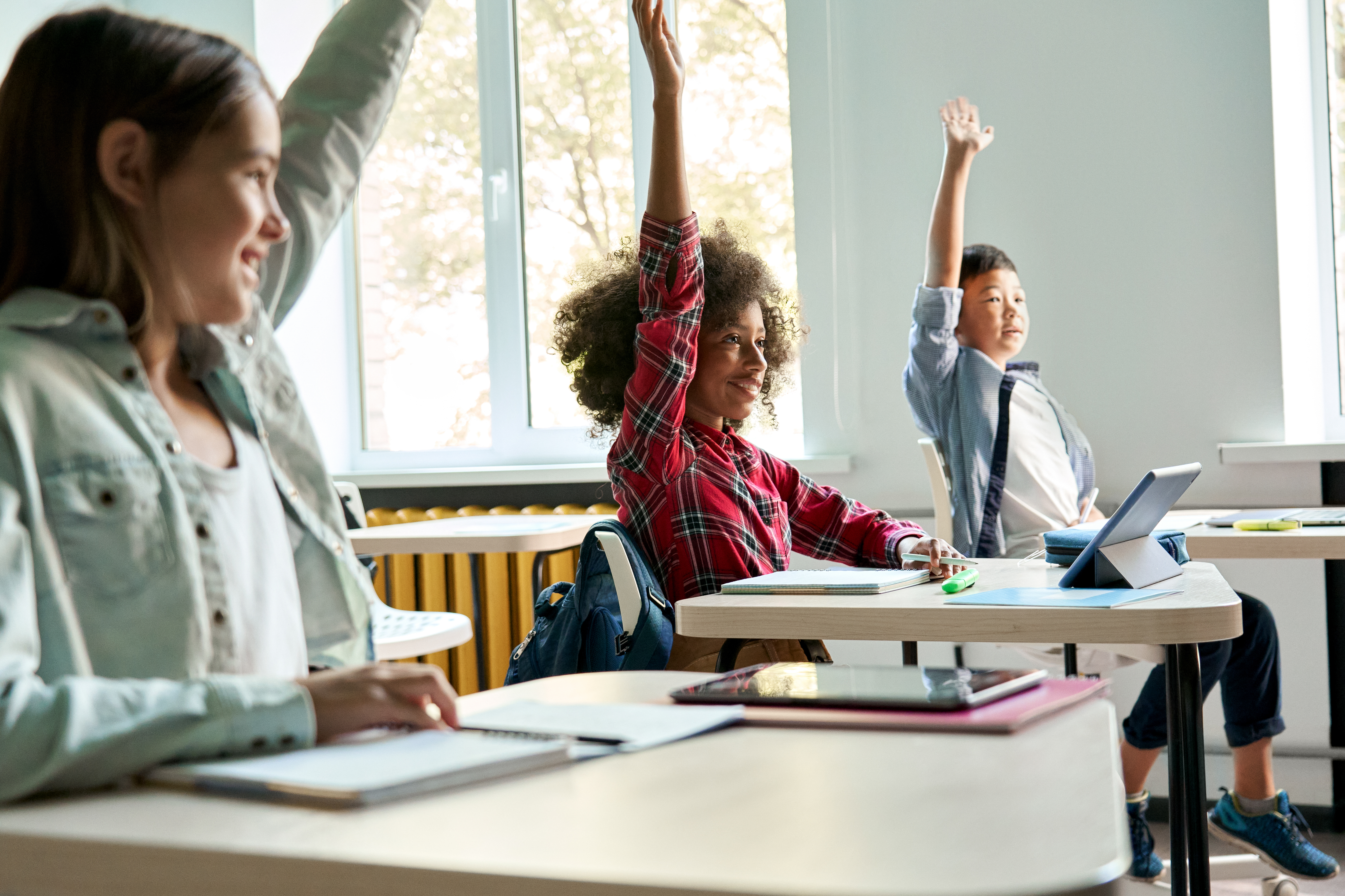 Diverse Schoolkids Sitting At Desk Raising Hands A 3b3baa25f6fcabec9eb9