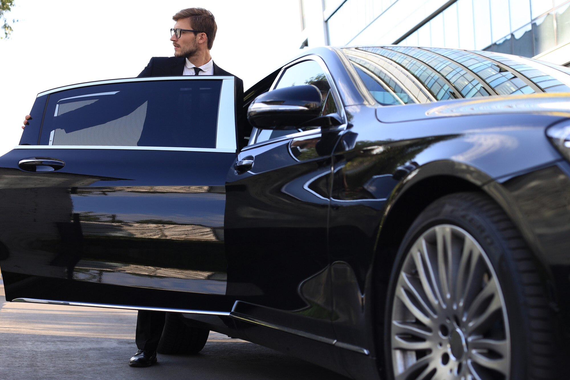 Elegant young businessman in a suit opening the door of a luxury black car, reflecting a premium travel experience with Angel's Chauffeurs in Adelaide.