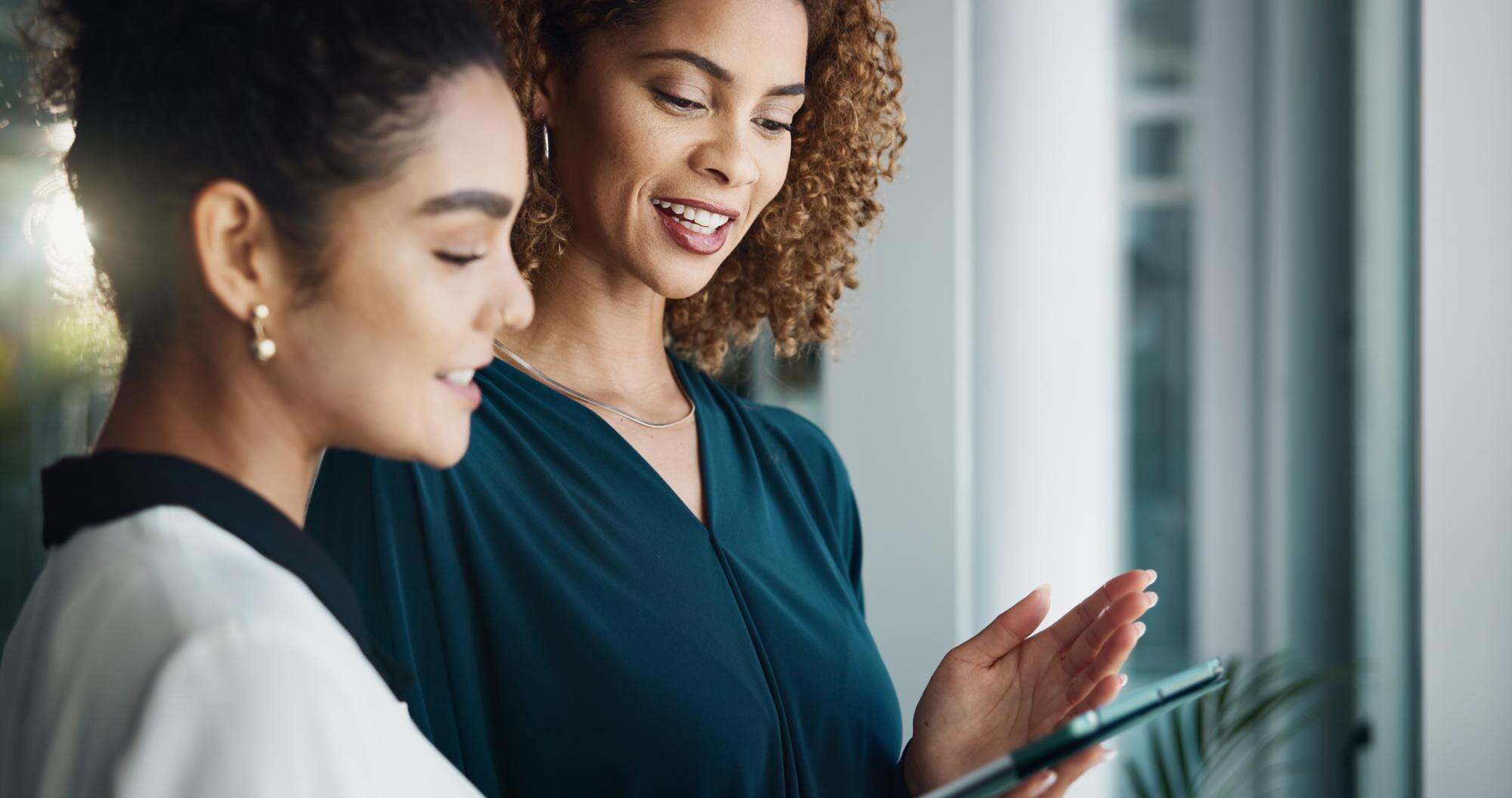 Two women collaborating in an office setting, discussing insights on a tablet, highlighting teamwork and engagement in managing online reviews and Google Business Profiles.