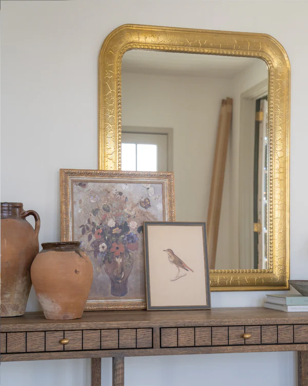 An assortment of vintage inspired artwork featuring farm animals and landscapes resting against a cupboards in a orange and white checkered floor in a farmhouse kitchen.
