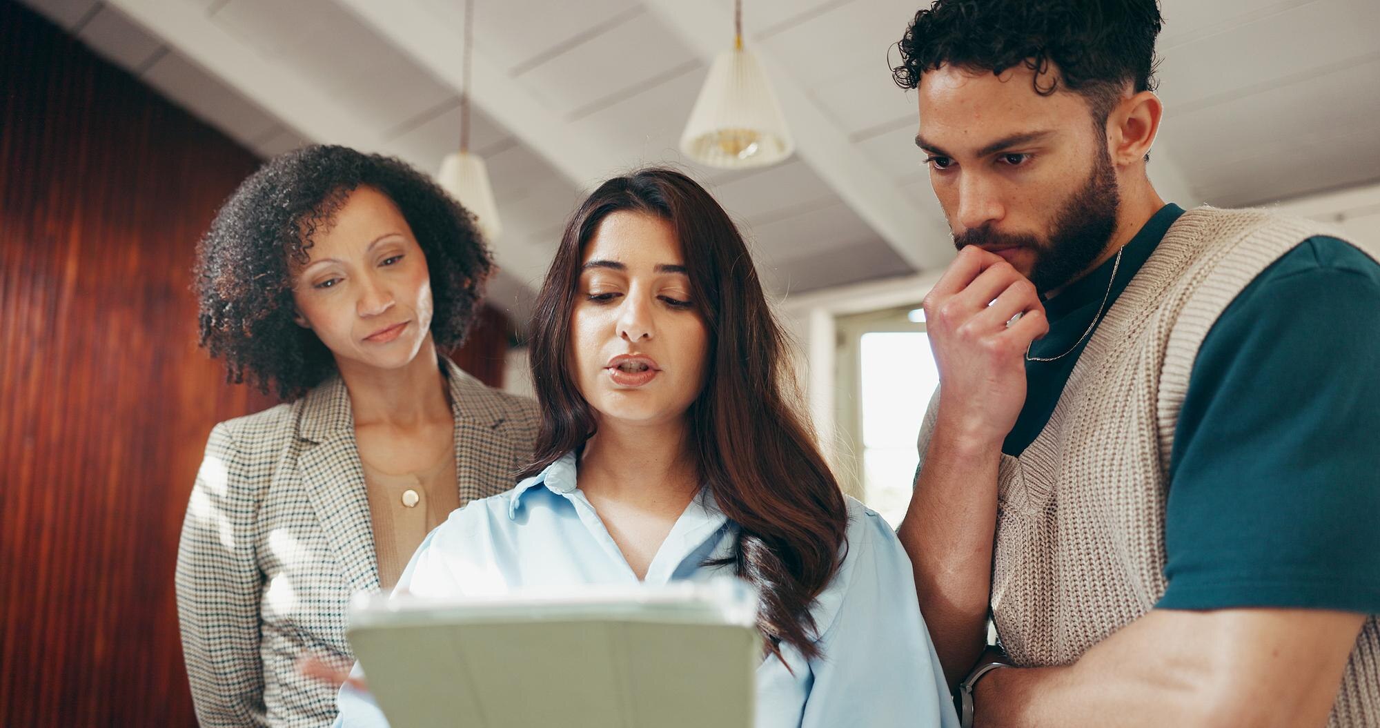 Group of business professionals collaborating and discussing ideas while reviewing a tablet in a modern office setting.