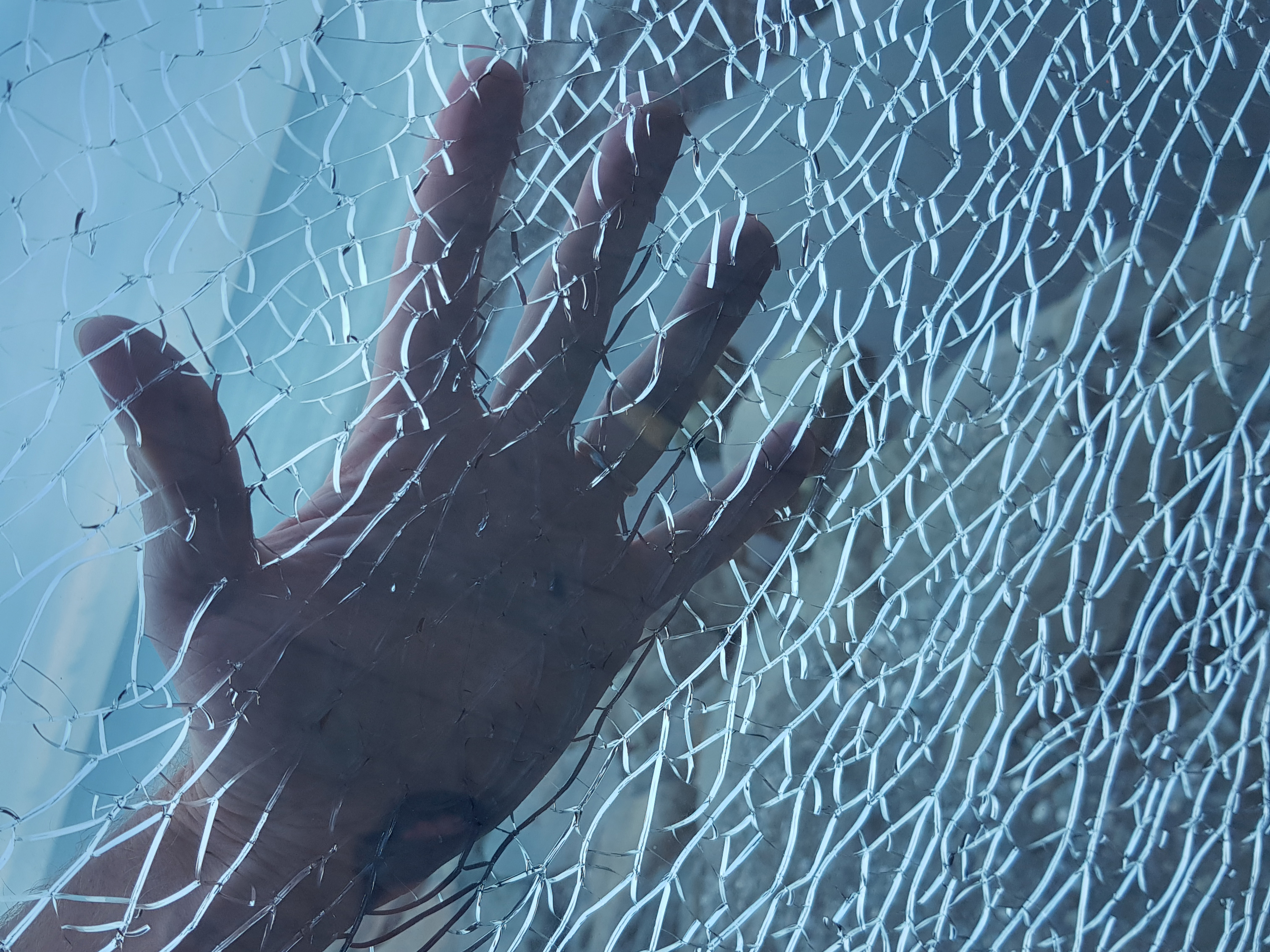 The hidden risks of imprecise plastic cuts in construction and manufacturing 2 hand behind blue broken glass with white cracks 5499f727b944cab32a69