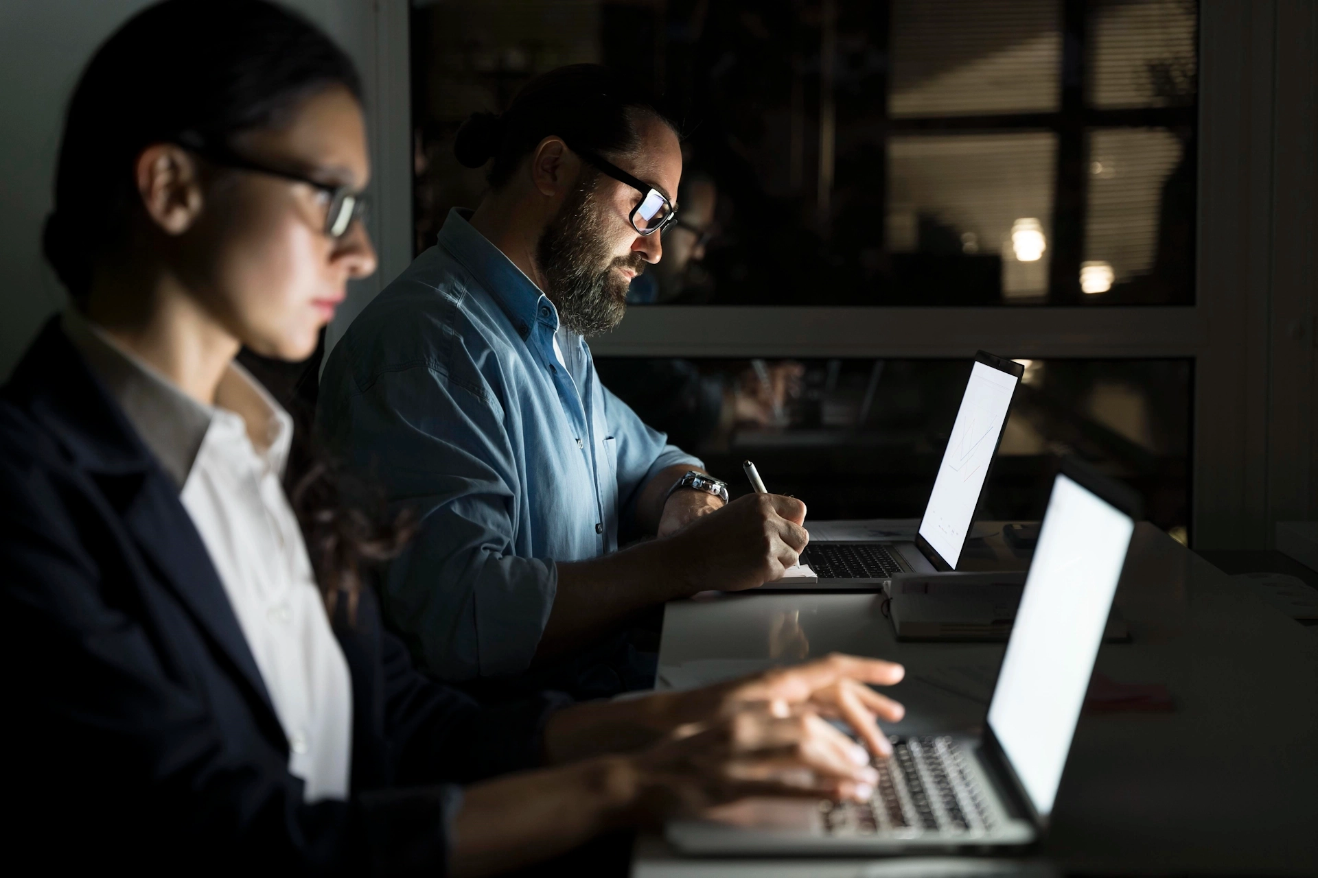 Professionals working on laptops in a dimly lit office, emphasizing collaboration and focus on managed IT services and cybersecurity solutions.