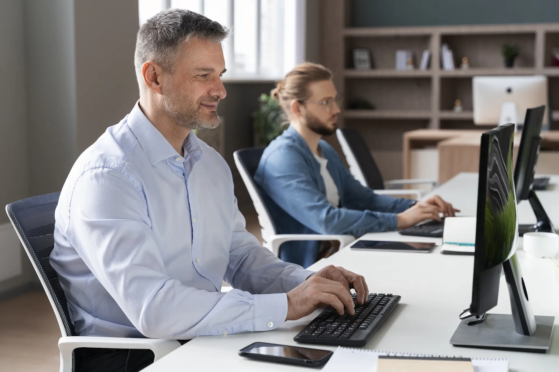 Business professionals working at computers in a modern office setting, demonstrating collaboration and productivity in IT environments.