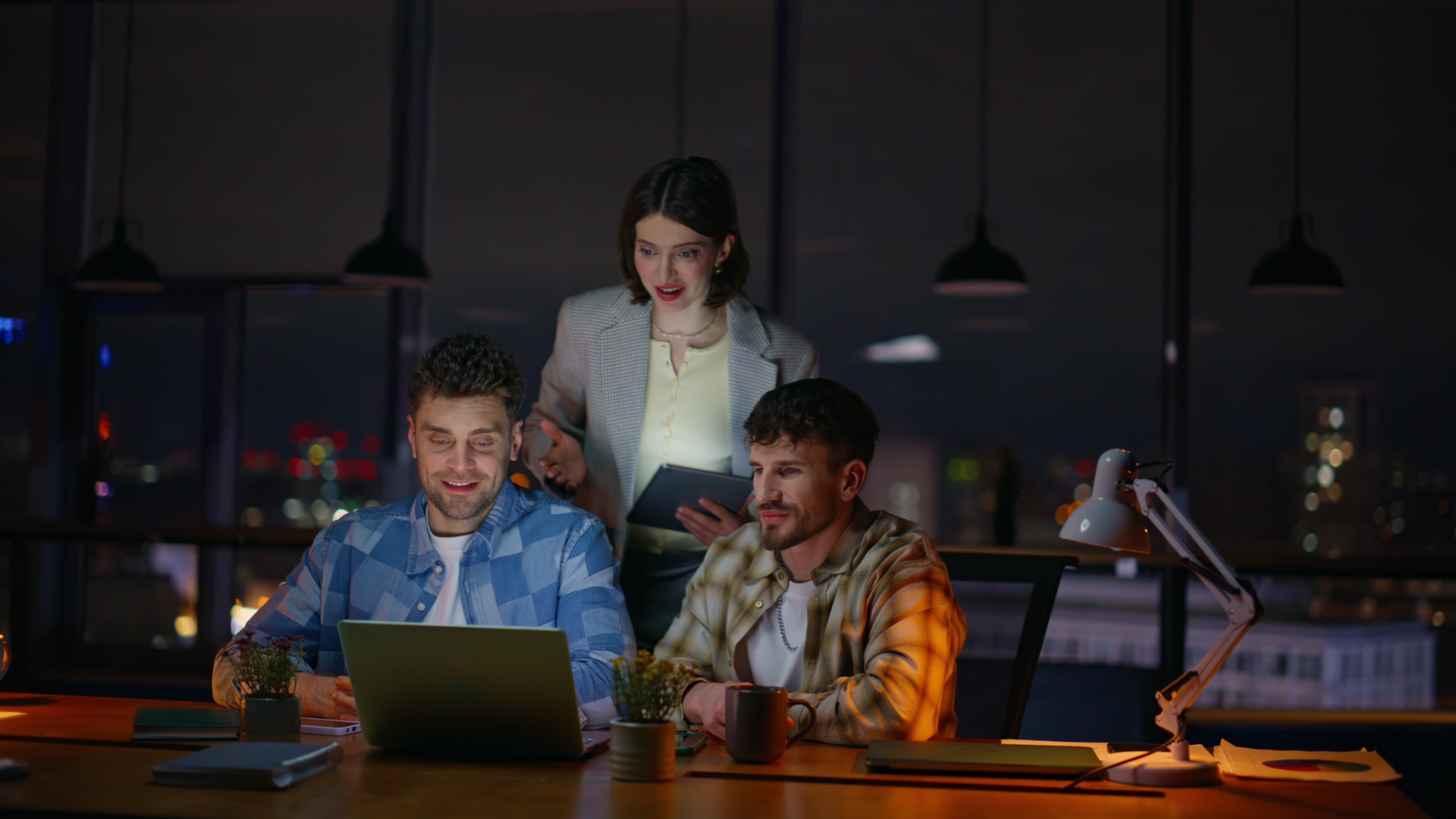 Three colleagues engaging in a video call on a laptop, discussing feedback and strategies for reputation management, in a modern office setting at night.