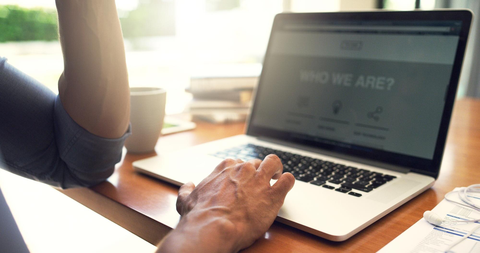 Person typing on a laptop showcasing website clarity with "Who We Are?" displayed on the screen, emphasizing digital engagement strategies.
