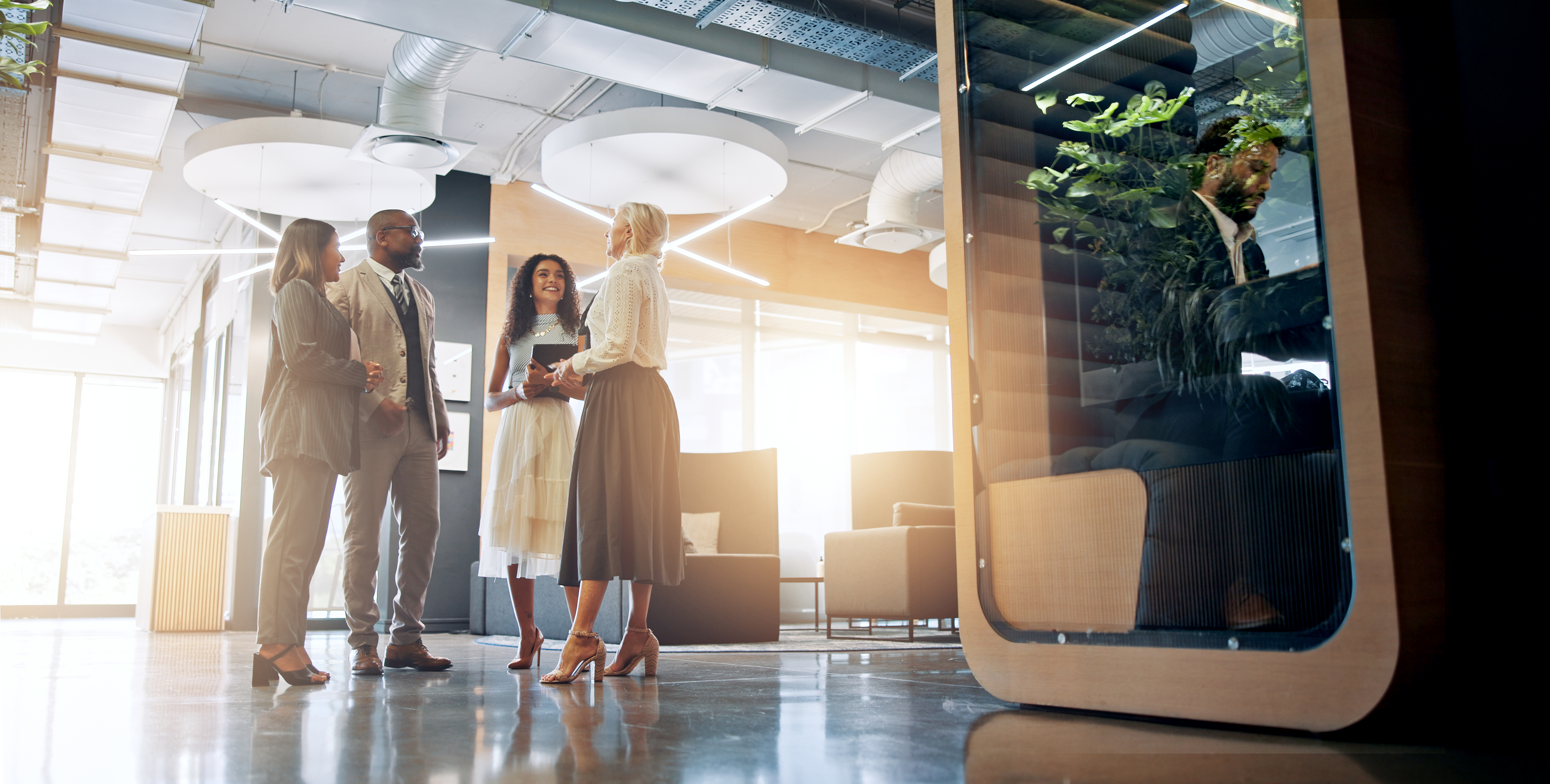 4 professionally dressed colleagues standing in an office common space chatting