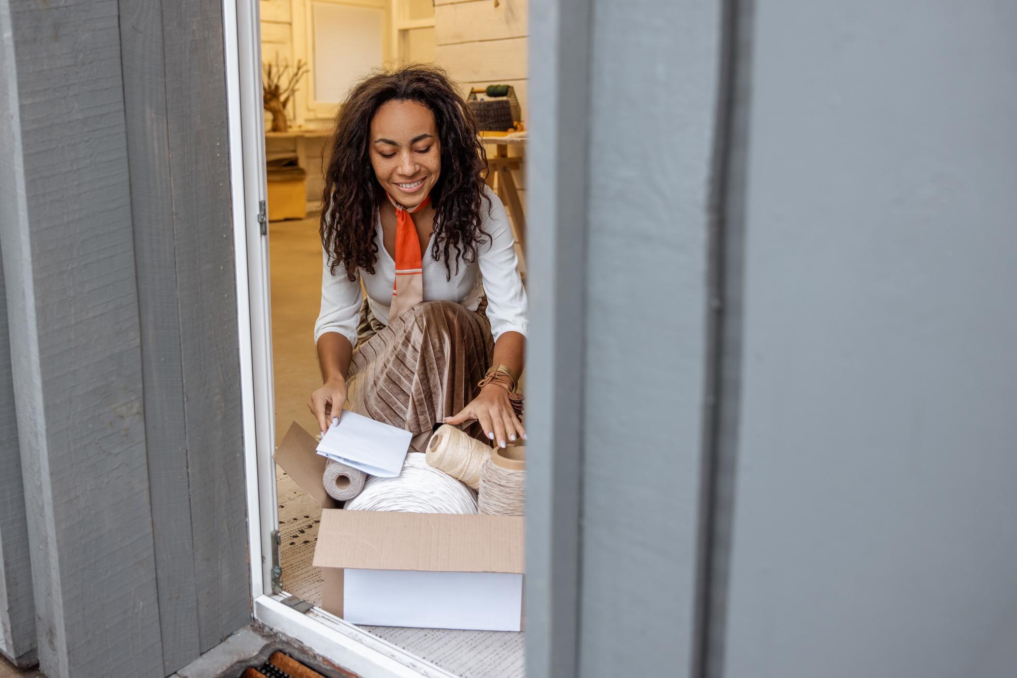 A woman crouches on the floor to look through a box of crochet string and hemp.