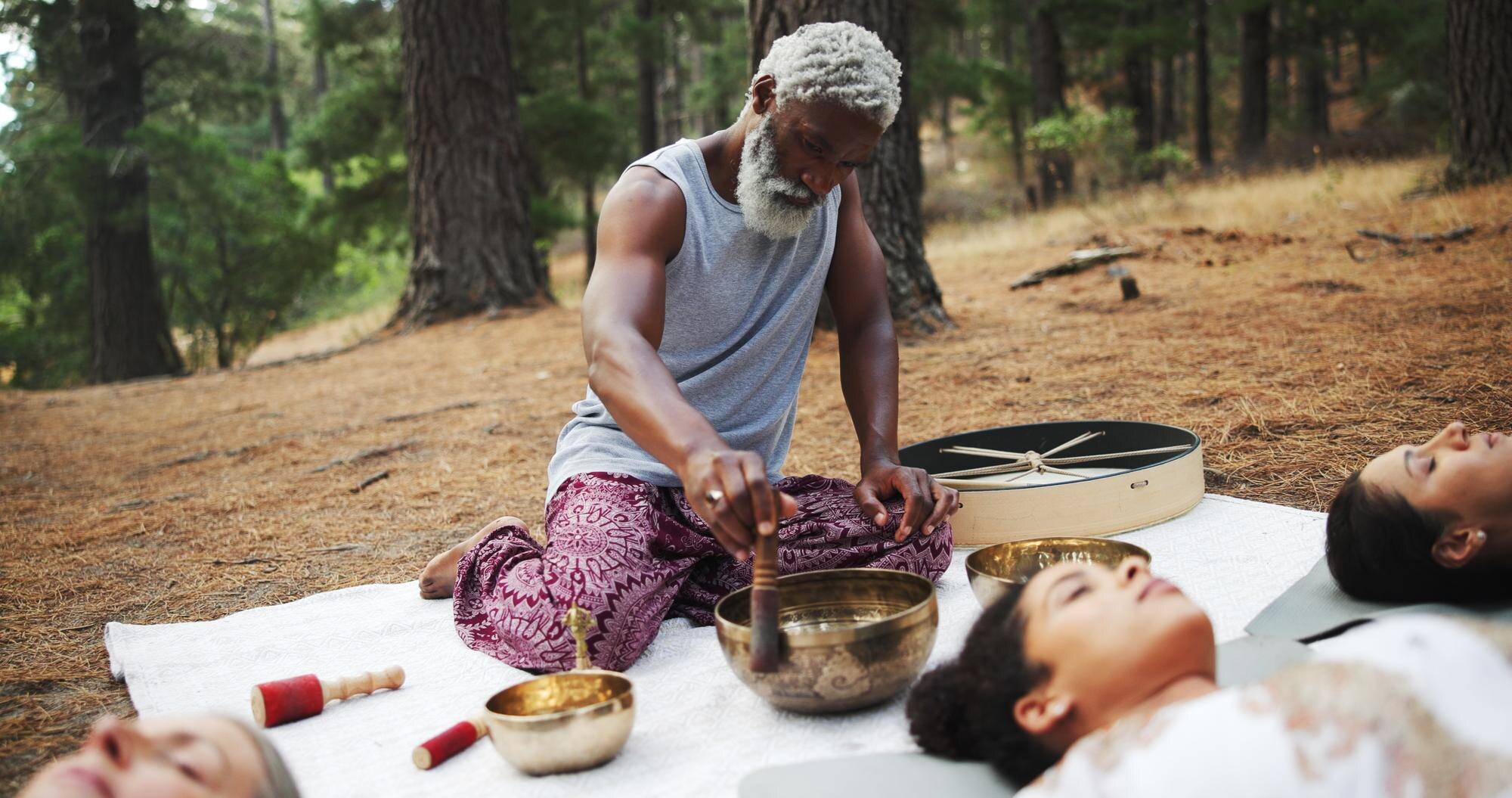 Man performing a sound healing meditation with singing bowls for a group during an outdoor forest wellness session. Nature-Led Experiences