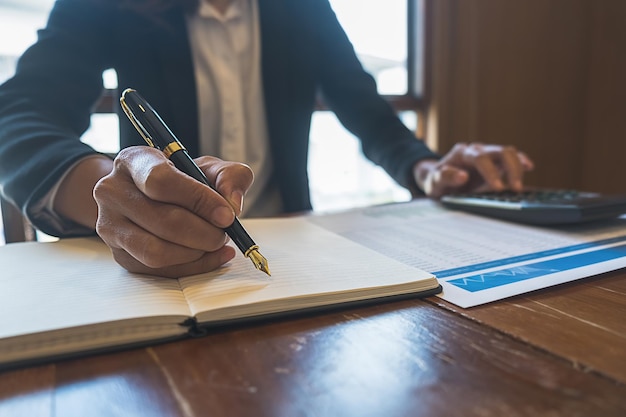 Businesswoman writing notes in a notebook while working at a desk with a calculator and financial documents, emphasizing the importance of contracts and compliance for small business legal strategies.