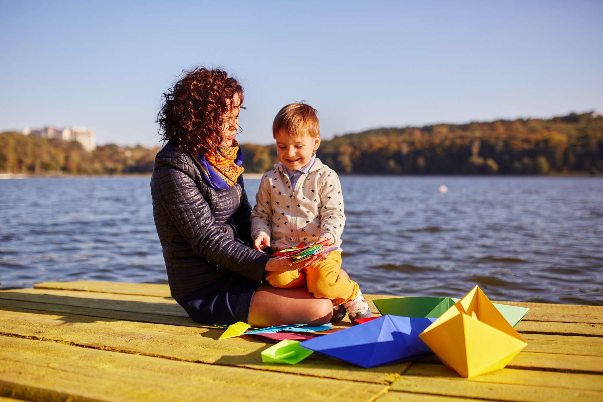 mom and son playing with paper boats by the lake 934087a93311bbb35cca