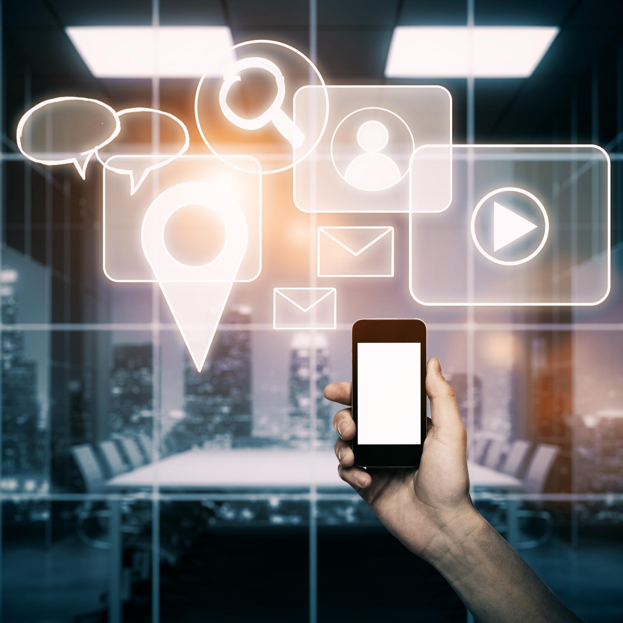 Hand holding smartphone with digital icons representing communication, location, and media, set in a modern office environment, illustrating strategies for enhancing customer engagement and visibility on Google Business Profiles.