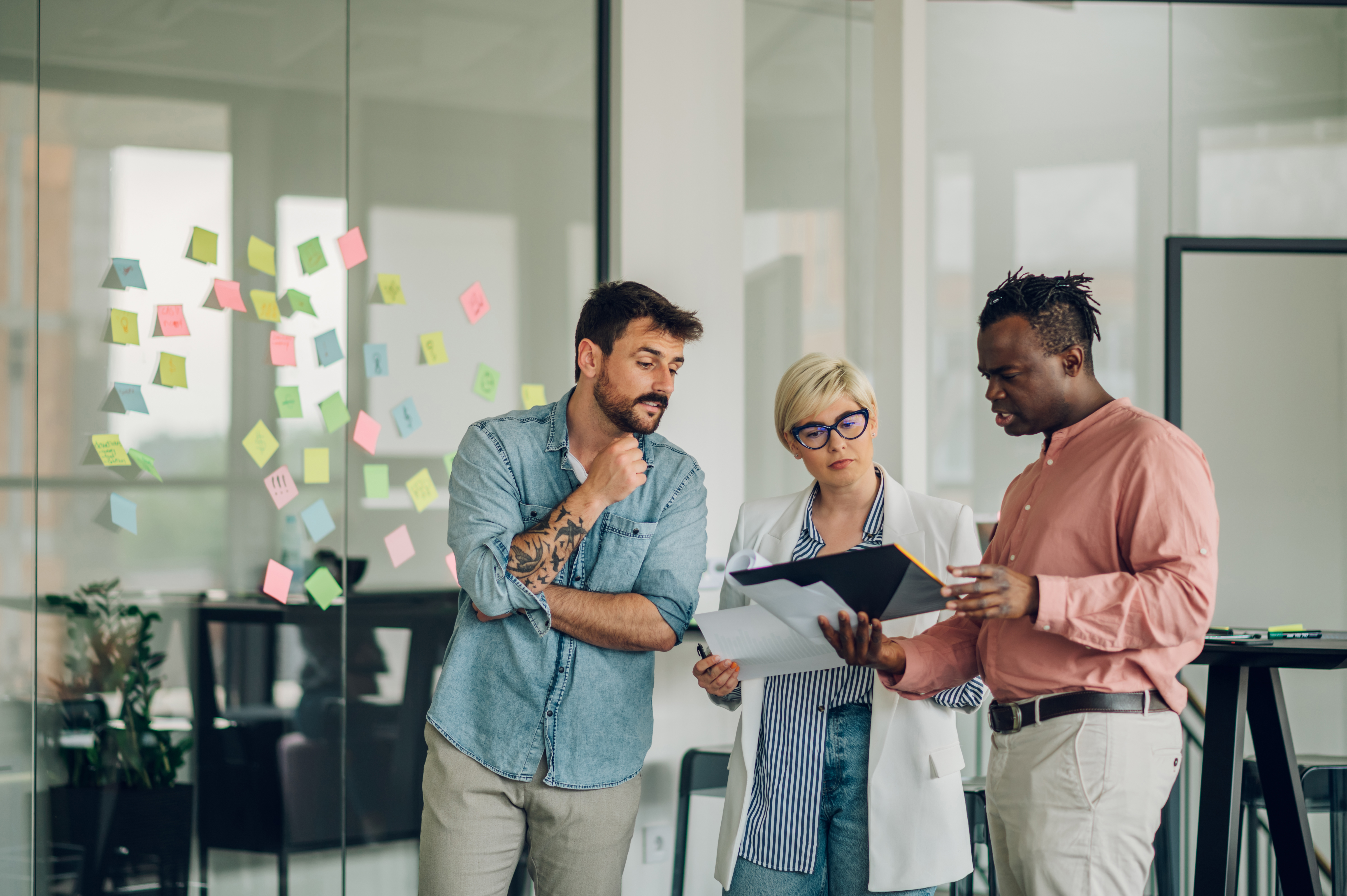 Multiracial business colleagues discussing documents in a modern office, surrounded by colourful sticky notes, emphasising collaboration and effective communication for reputation management and local SEO strategies.