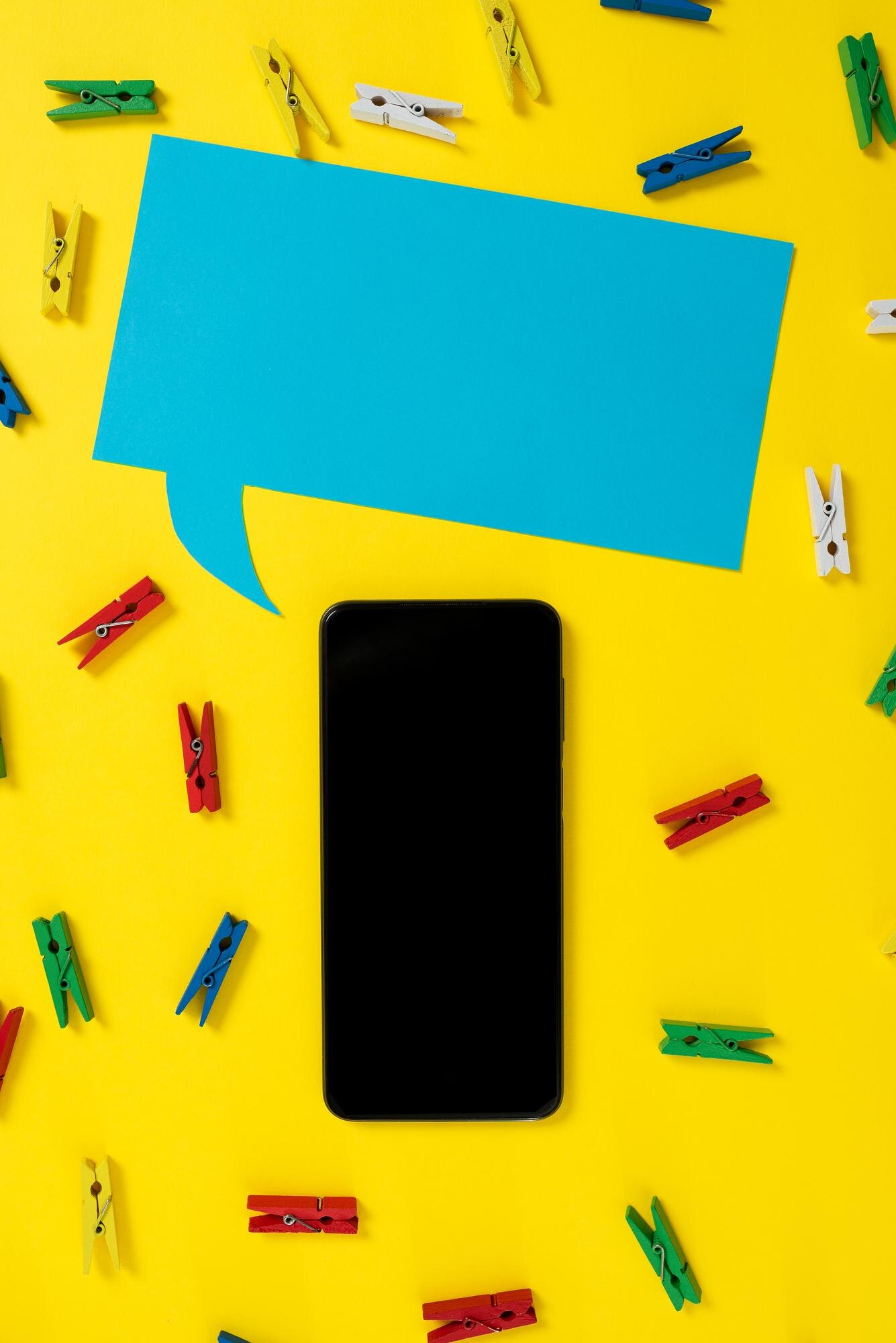 Smartphone surrounded by colourful clothespins and a blue speech bubble, symbolising communication and digital presence in local SEO context.