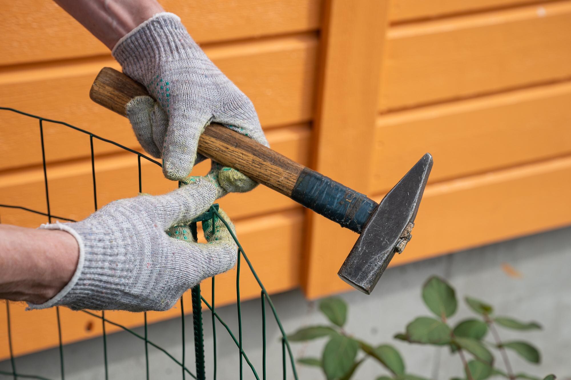 Person Hammering Green Metal Fence Post With A Ste