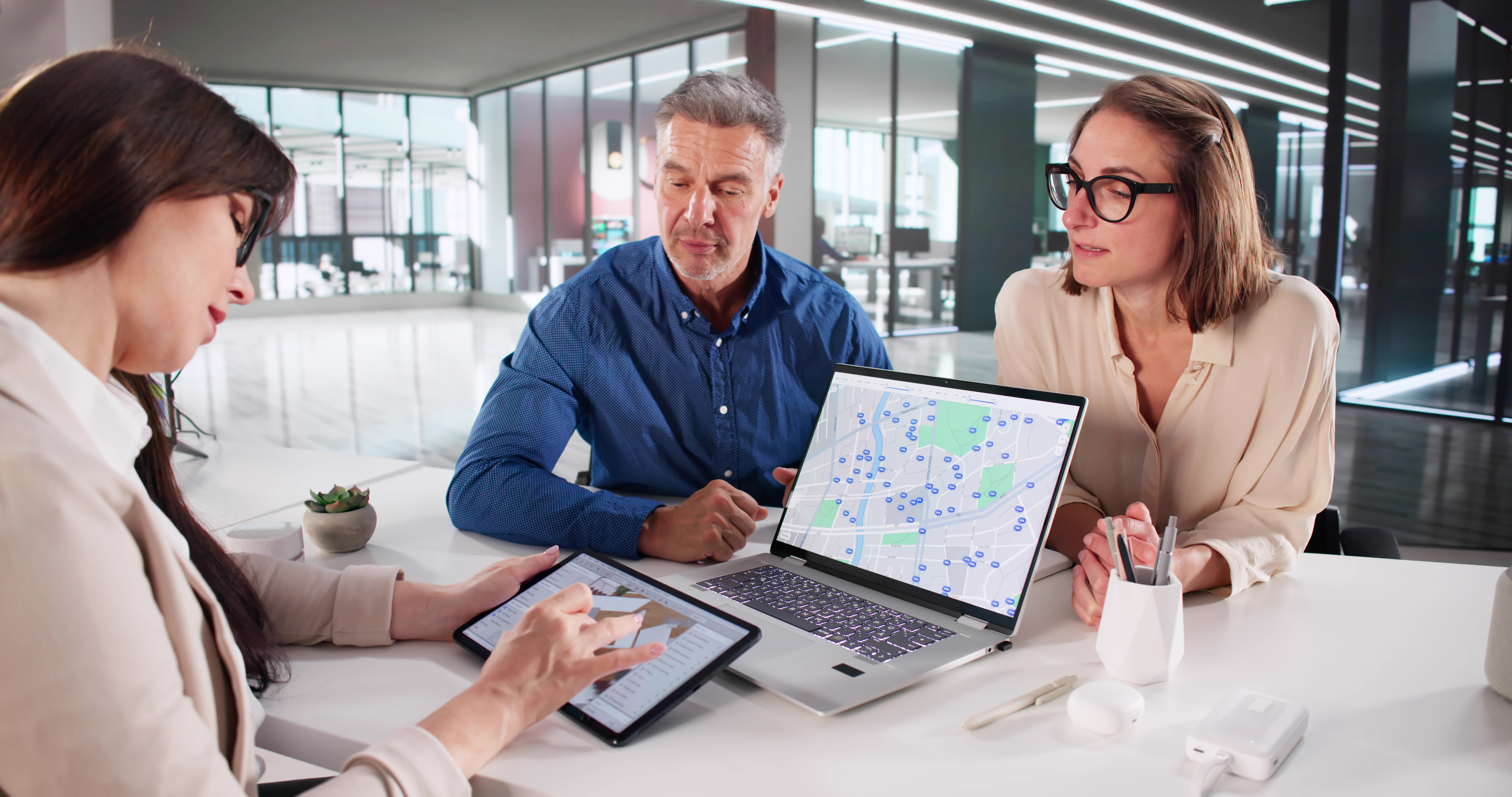 Group of professionals discussing local SEO strategies and service area expansion, with a laptop displaying a map and analytics data on a modern office table.