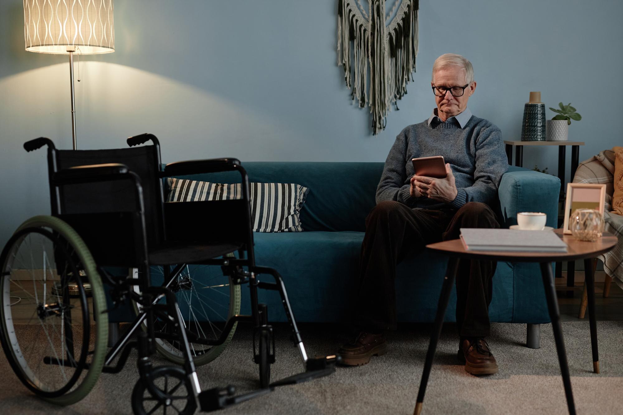senior wheelchair user sitting on couch typing on 58734ede5aa6de2a4766
