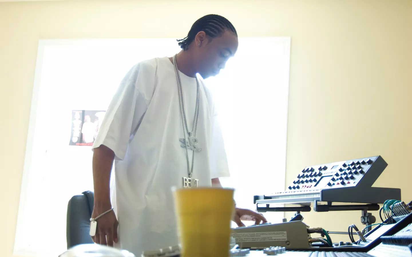 Aspiring music producer working in a home studio, adjusting synth gear and drum machines in a sunlit room—early-stage trap beat creation setup.