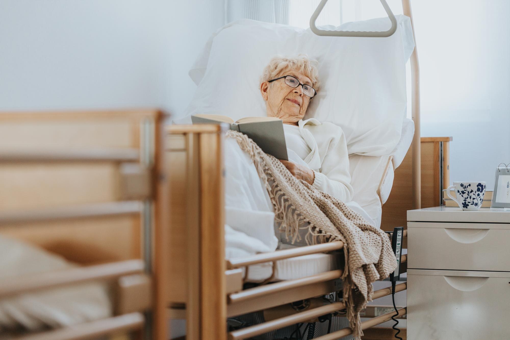 sick senior woman lies in a hospital bed and reads eeb5a2a62b6bd5aef4bc