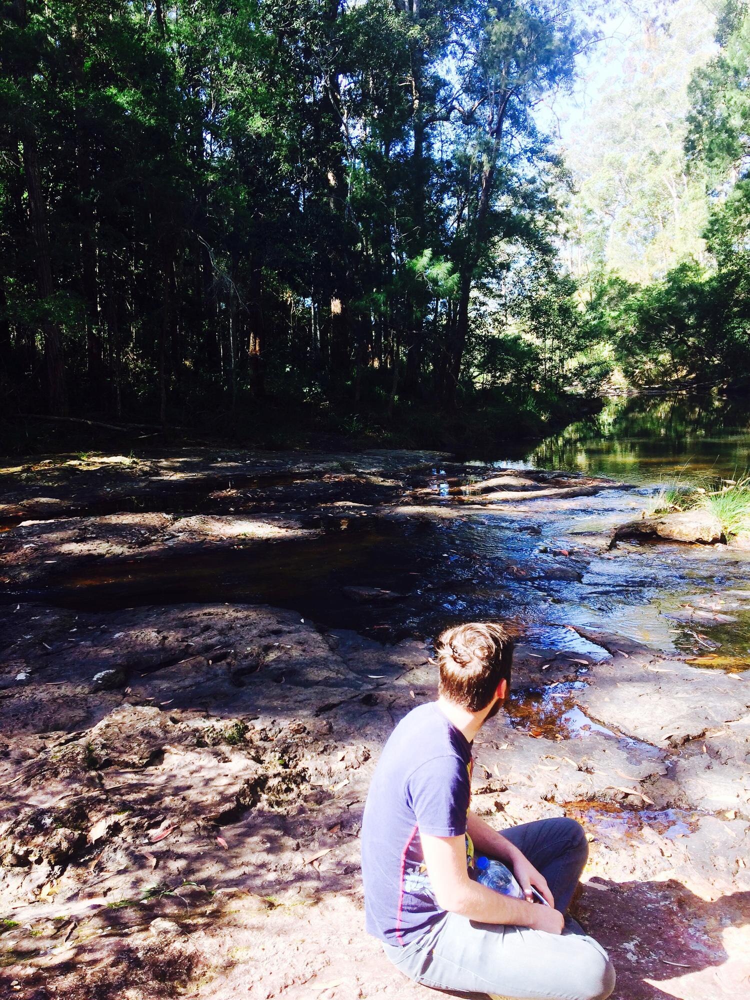 side view of man sitting at riverbank in forest f0d0a96ff442ed867c02