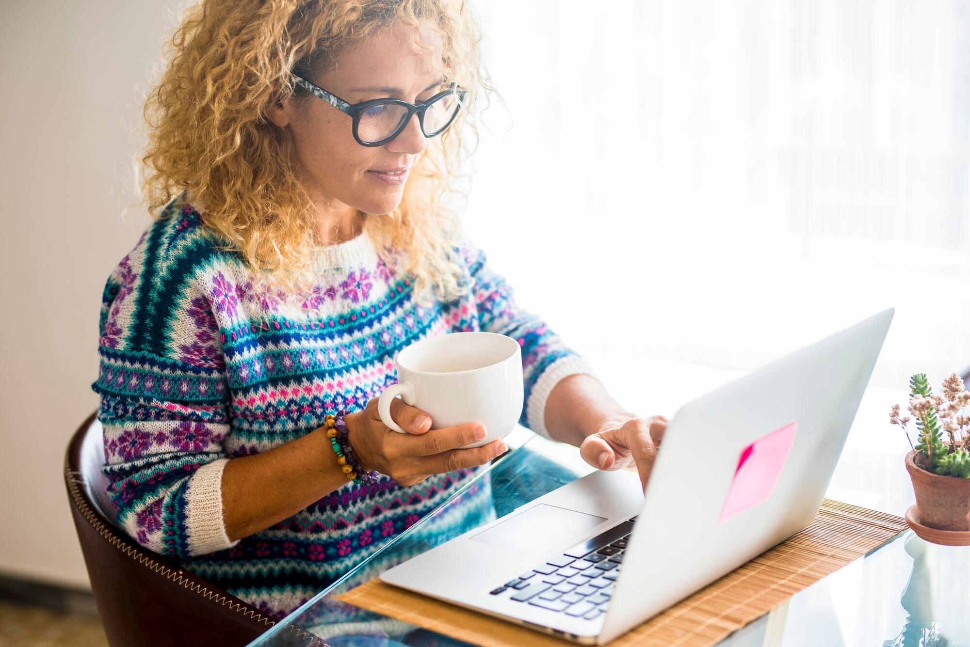 smiling woman holding coffee cup while working on a894ace07d53248f9d64