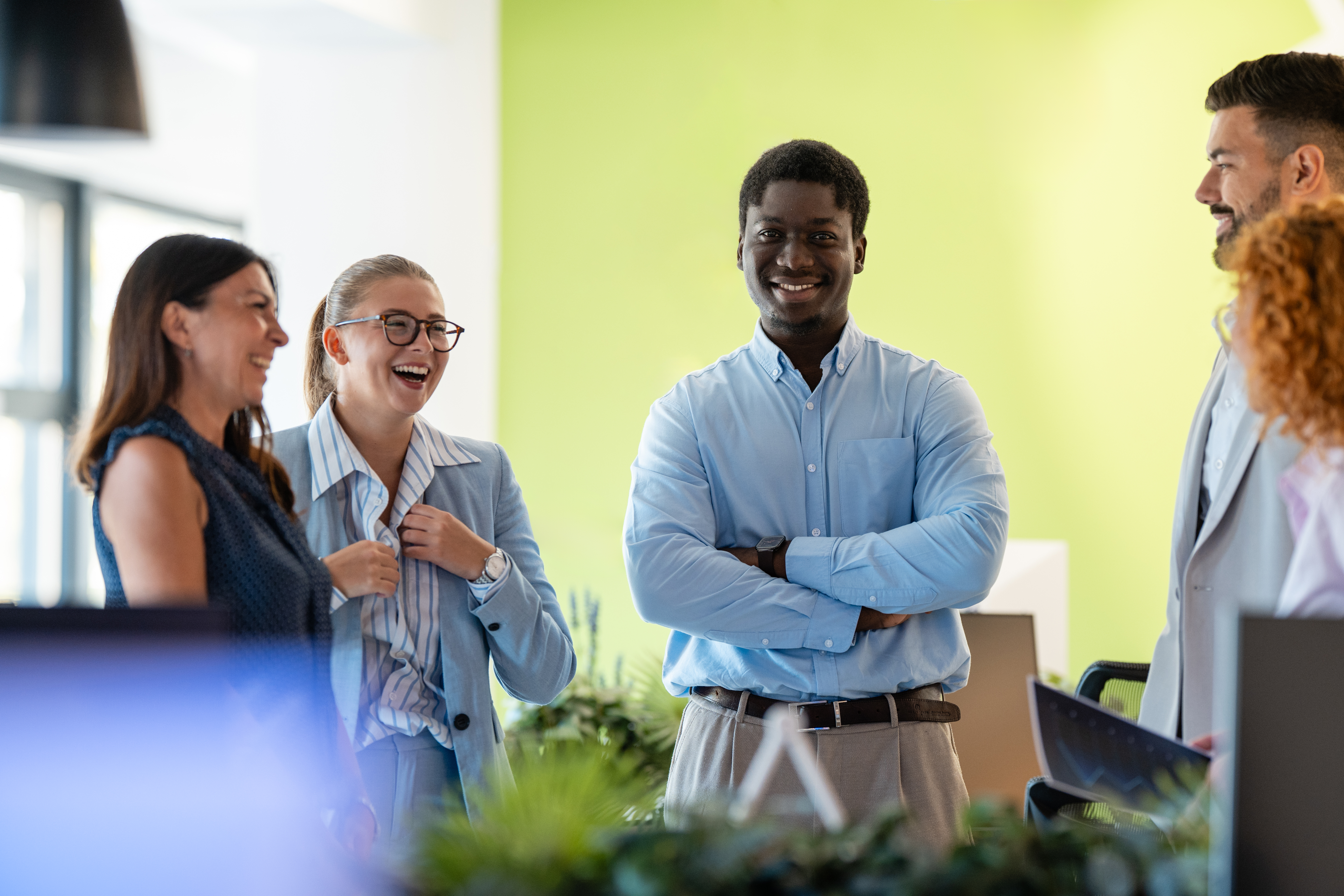 a man standing with his arms crossed while smiling and talking with coworkers