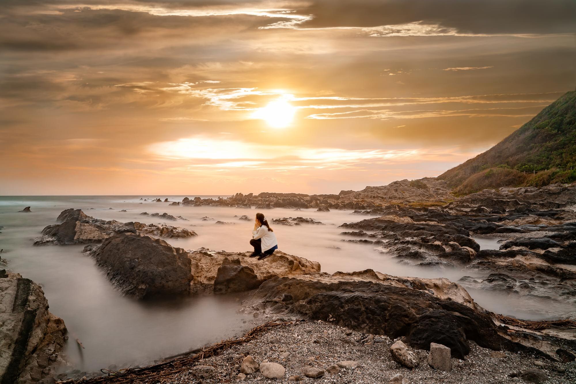 teenage girl sitting on rock at beach against sky d9aee1dbcafac73cc23f BTOURS