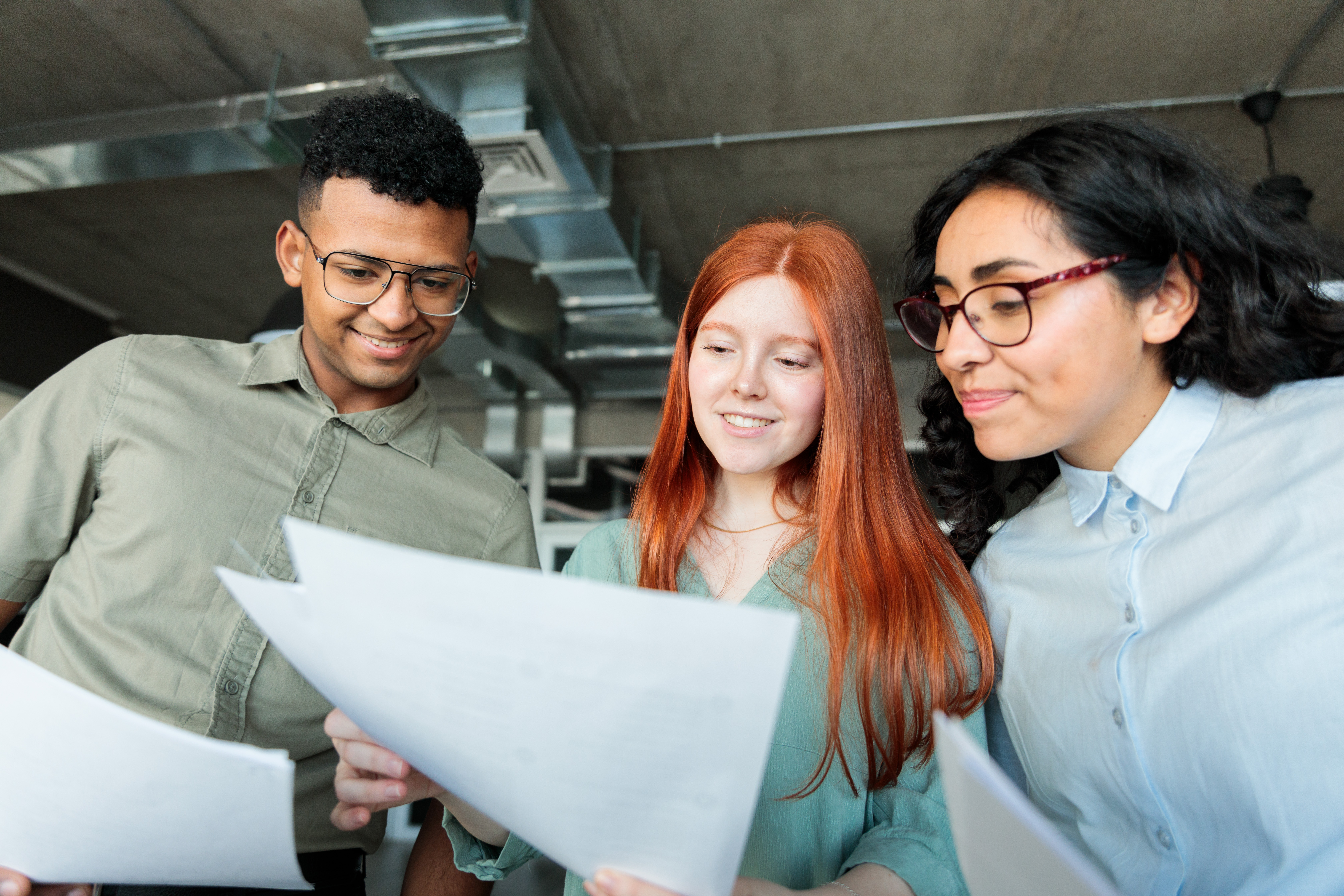 Three young Latin coworkers reviewing documents in a modern office setting, emphasizing collaboration and contract discussions relevant to small business legal strategies.