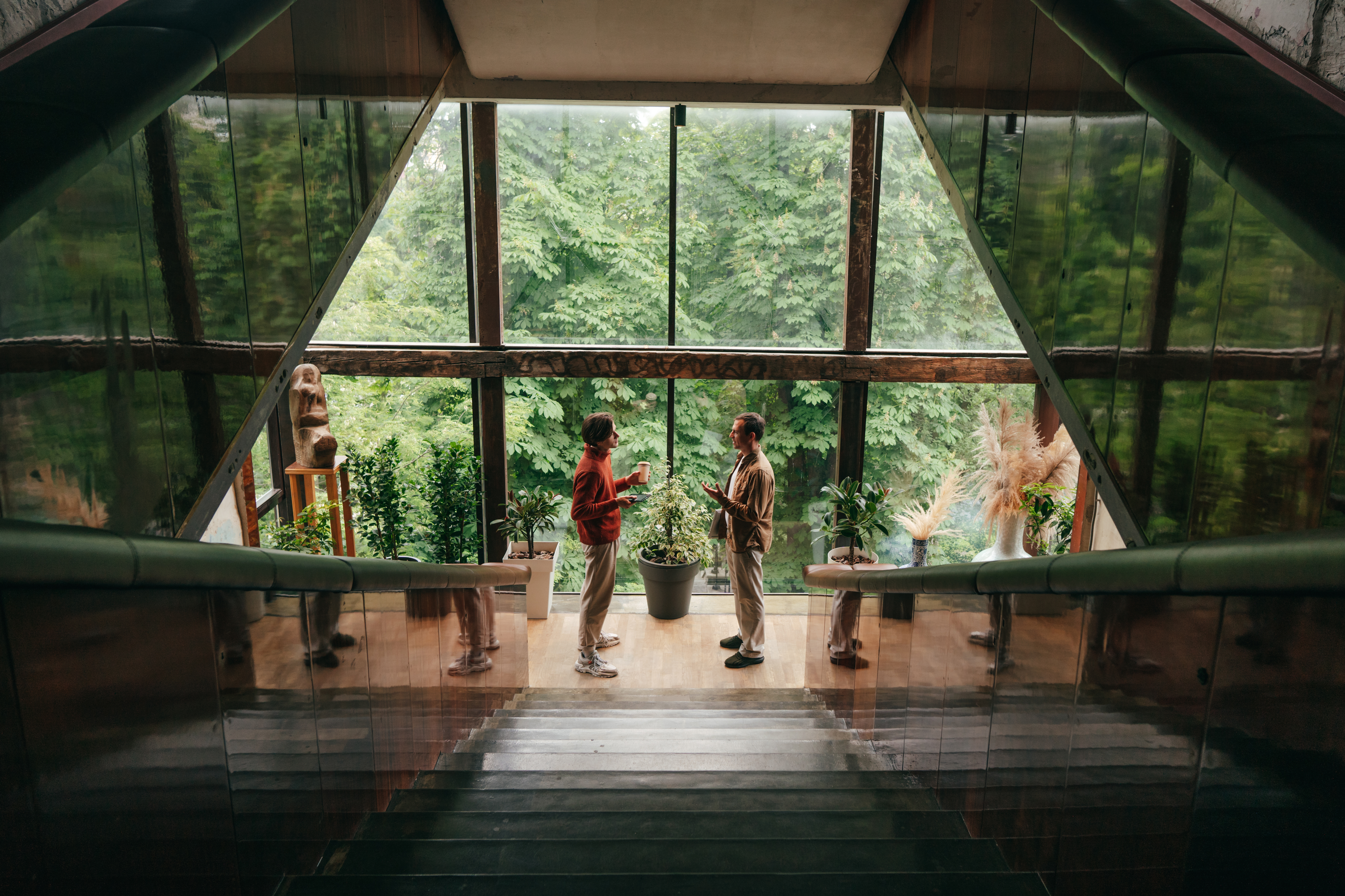 People talking inside a modern glass building surrounded by lush green forest nature.