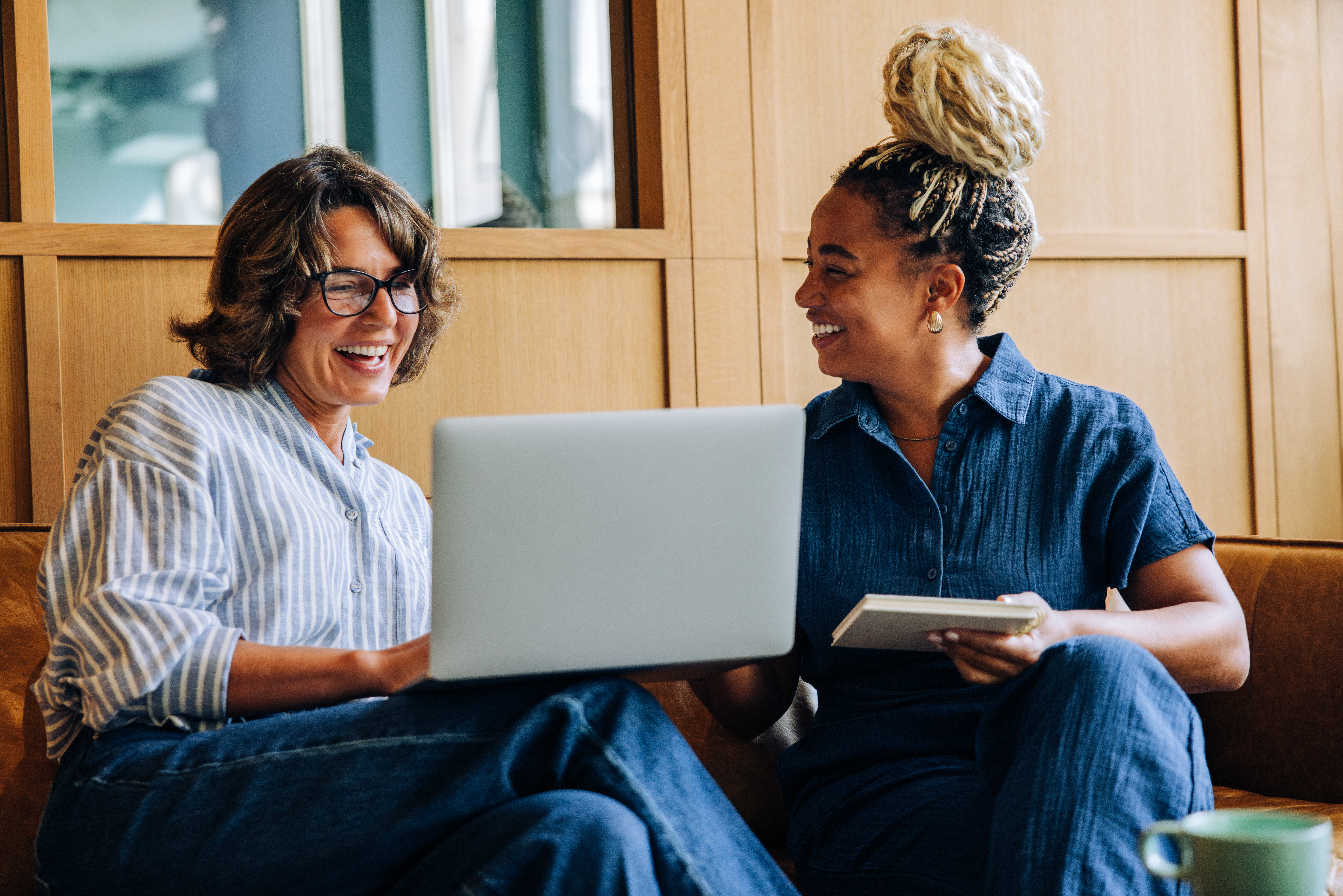two women smiling while using a laptop and notepad c420293875c5b06777b3