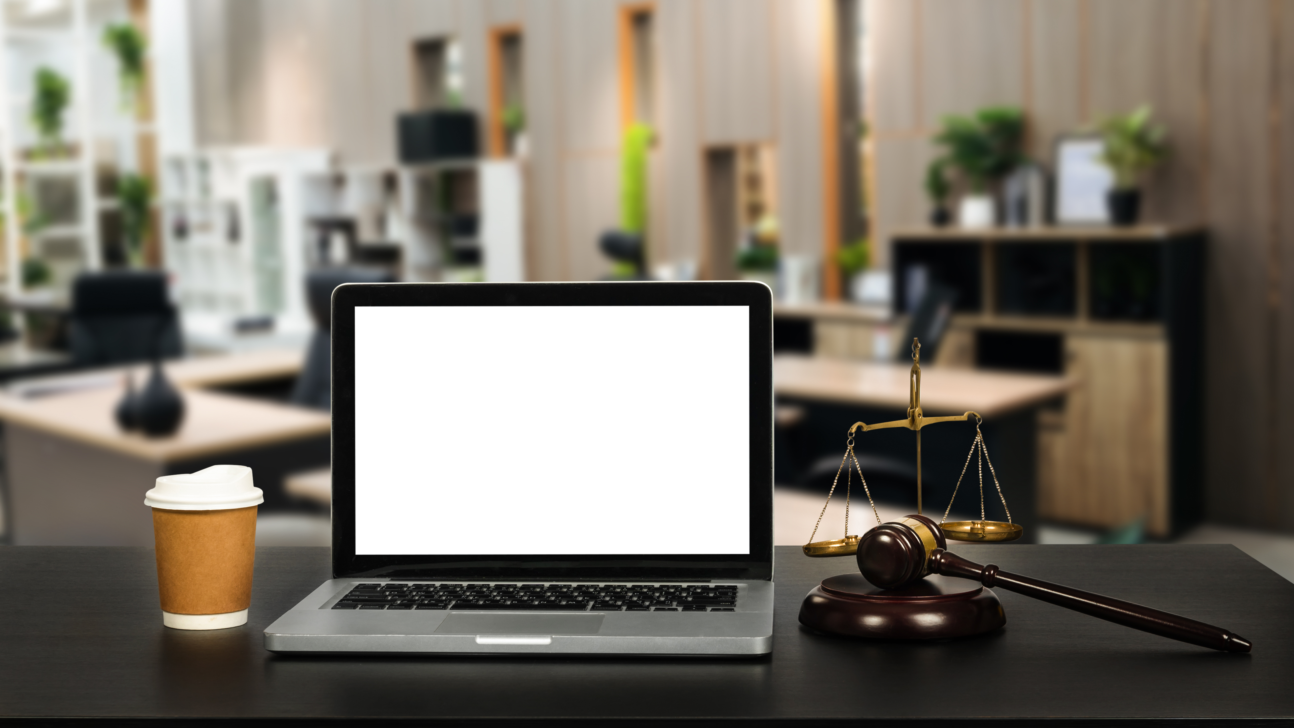 Laptop with blank screen, gavel, and scales of justice on desk in a modern office setting, symbolizing legal compliance and support for small businesses.